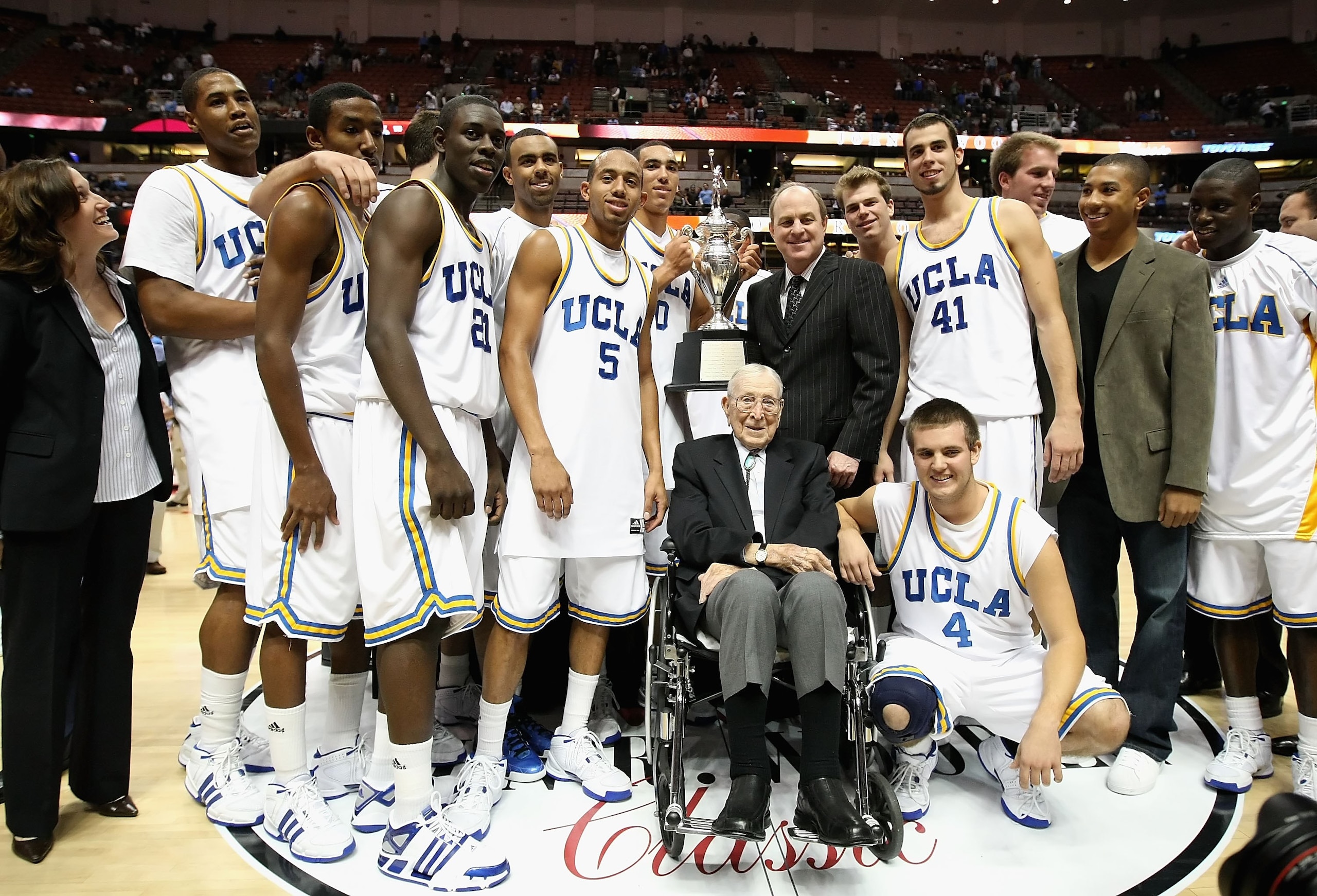 ANAHEIM, CA - DECEMBER 13:  Former coach John Wooden poses together with the UCLA Bruins team, head coach Ben Howland and great grandson Tyler Trapani #4 after the John R. Wooden Classic game against the DePaul Blue Demons at Honda Center on December 13,