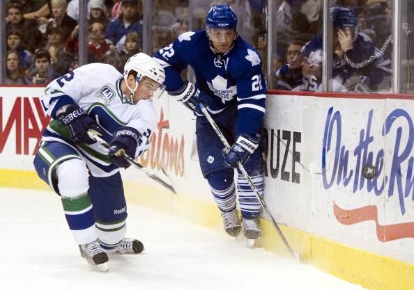 VANCOUVER, CANADA - DECEMBER 18:  Dan Hamhuis #2 of the Vancouver Canucks fires the puck out of his zone before getting checked by Francois Beauchemin #22 of the Toronto Maple Leafs during the first period in NHL action on December 18, 2010 at Rogers Aren