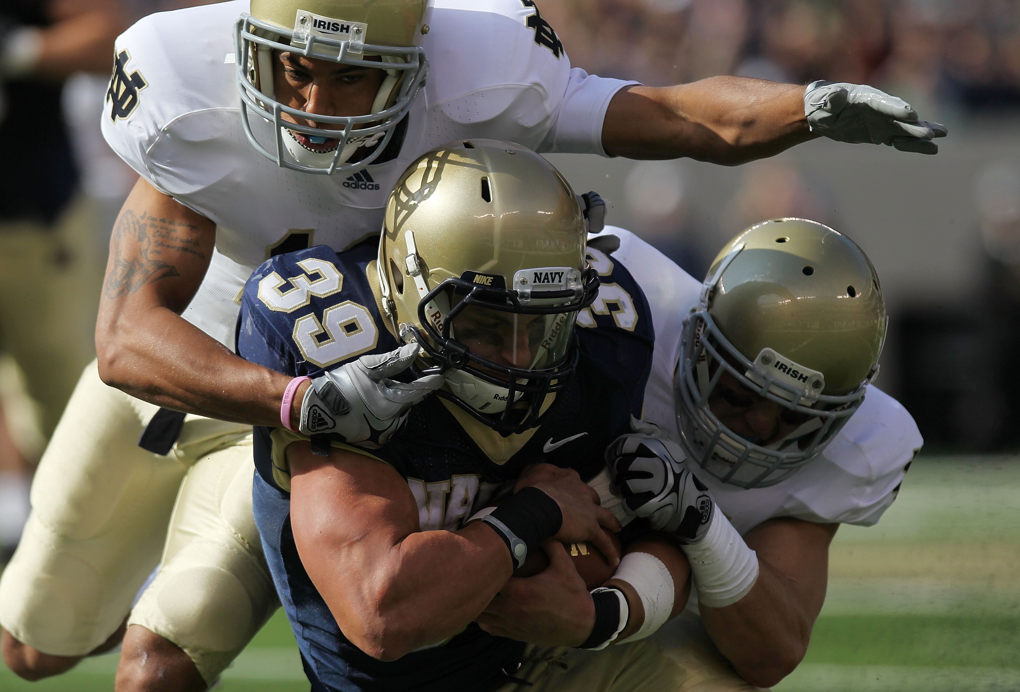 EAST RUTHERFORD, NJ - OCTOBER 23:  Alexander Teich #39 of the Navy Midshipmen is tackled by Robert Blanton #12 and Zeke Motta #17 of the Notre Dame Fighting Irish at New Meadowlands Stadium on October 23, 2010 in East Rutherford, New Jersey.  (Photo by Ni