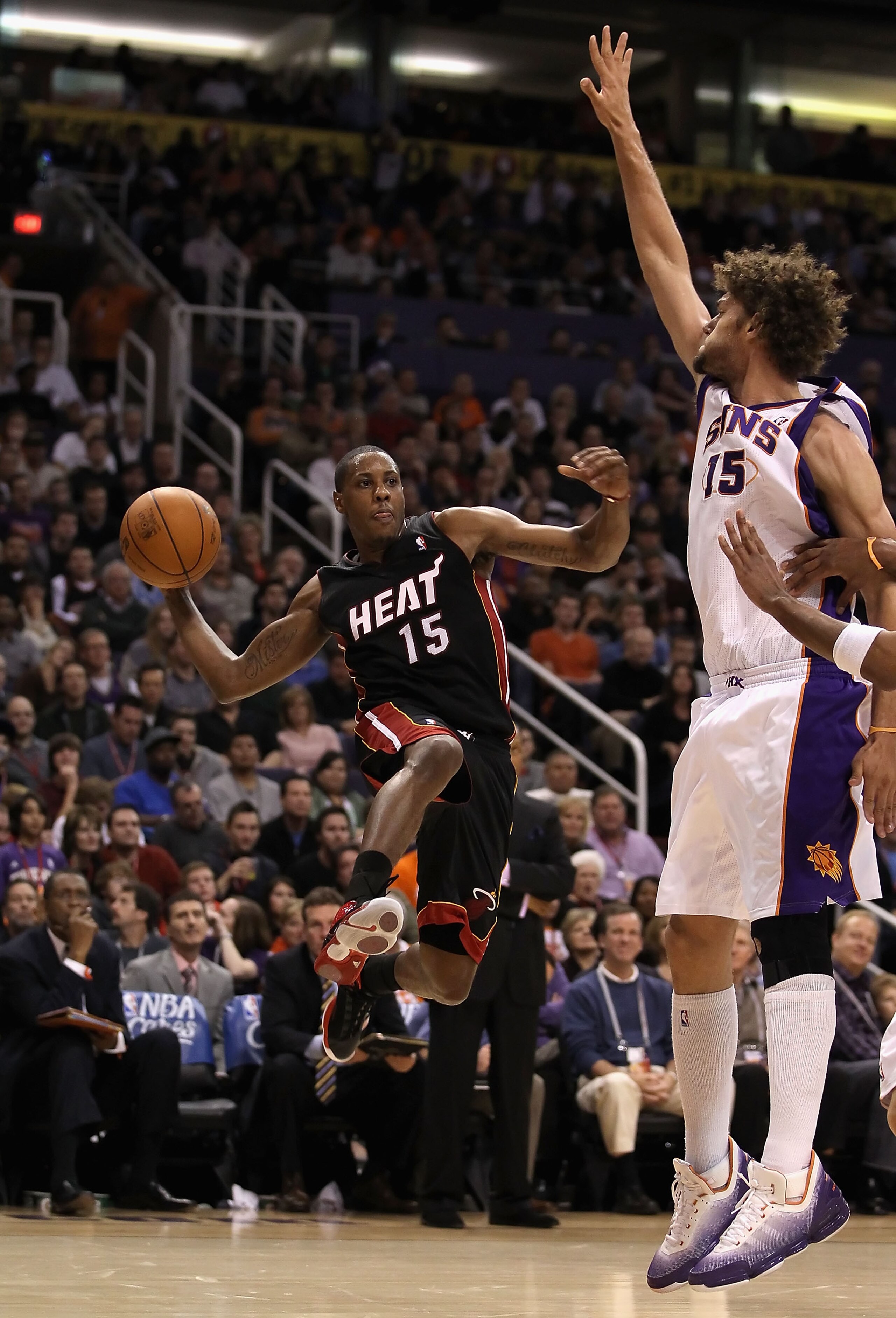 PHOENIX - DECEMBER 23: Mario Chalmers #15 of the Miami Heat passes the ball around Robin Lopez #15 of the Phoenix Suns during the NBA game at US Airways Center on December 23, 2010 in Phoenix, Arizona. The Heat defeated the Suns 95-83. NOTE TO USER: Use PHOENIX - DECEMBER 23: Mario Chalmers #15 of the Miami Heat passes the ball around Robin Lopez #15 of the Phoenix Suns during the NBA game at US Airways Center on December 23, 2010 in Phoenix, Arizona. The Heat defeated the Suns 95-83. NOTE TO USER: Use