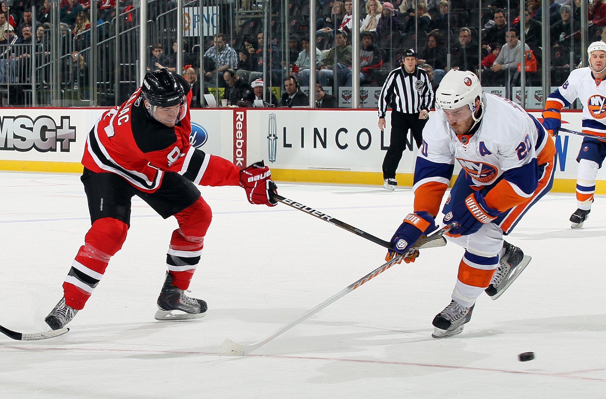 NEWARK, NJ - DECEMBER 23:  Travis Zajac #19 of the New Jersey Devils skates against James Wisniewski #20 of the New York Islanders at the Prudential Center on December 23, 2010 in Newark, New Jersey. The Isles defeated the Devils 5-1.  (Photo by Jim McIsa