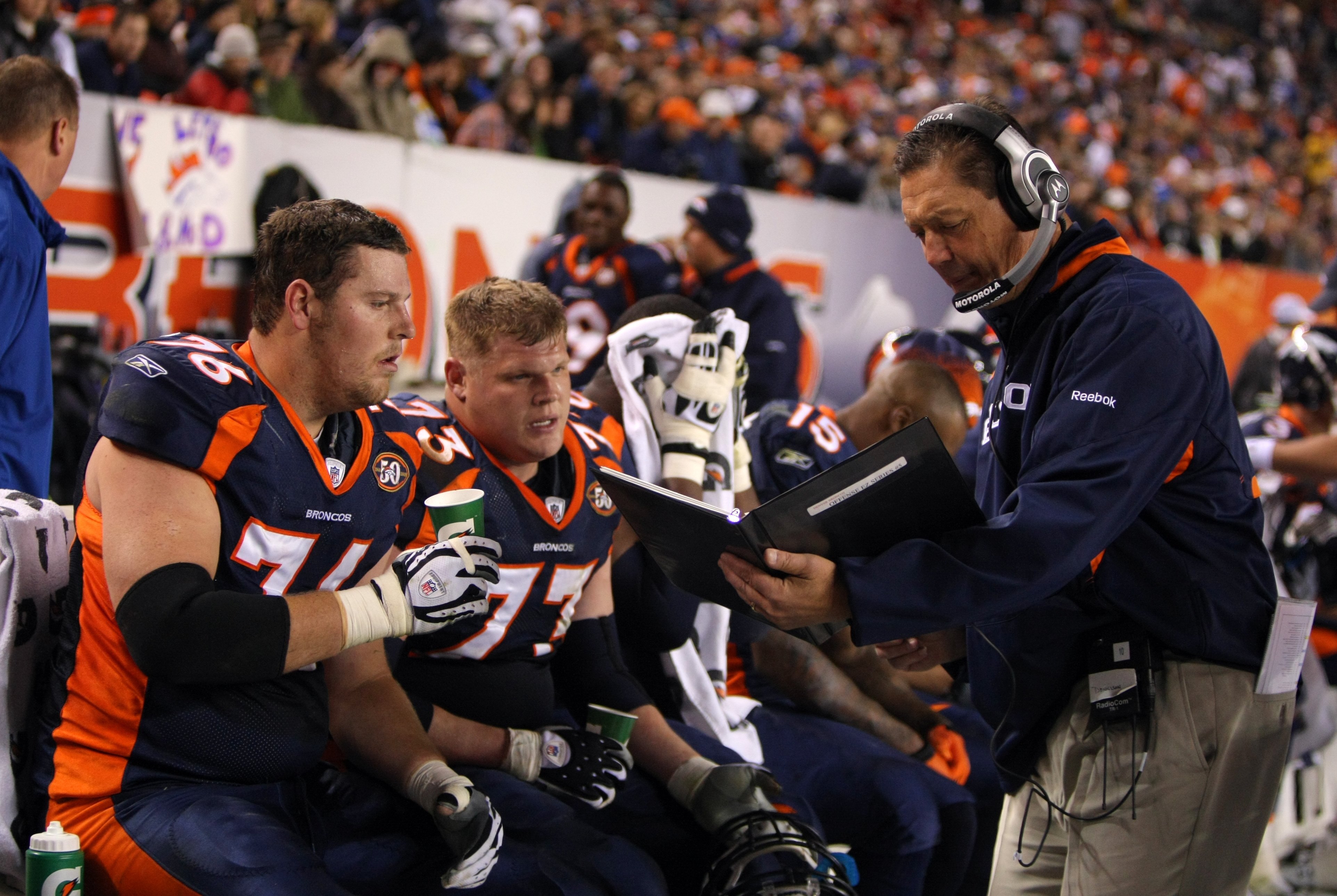 DENVER - NOVEMBER 26:  Offensive line coach Rick Dennison and Chris Kuper #73 and Tyler Polumbus #76 of the Denver Broncos look over photos in the bench area during their NFL game against the New York Giants at Invesco Field at Mile High on November 26, 2