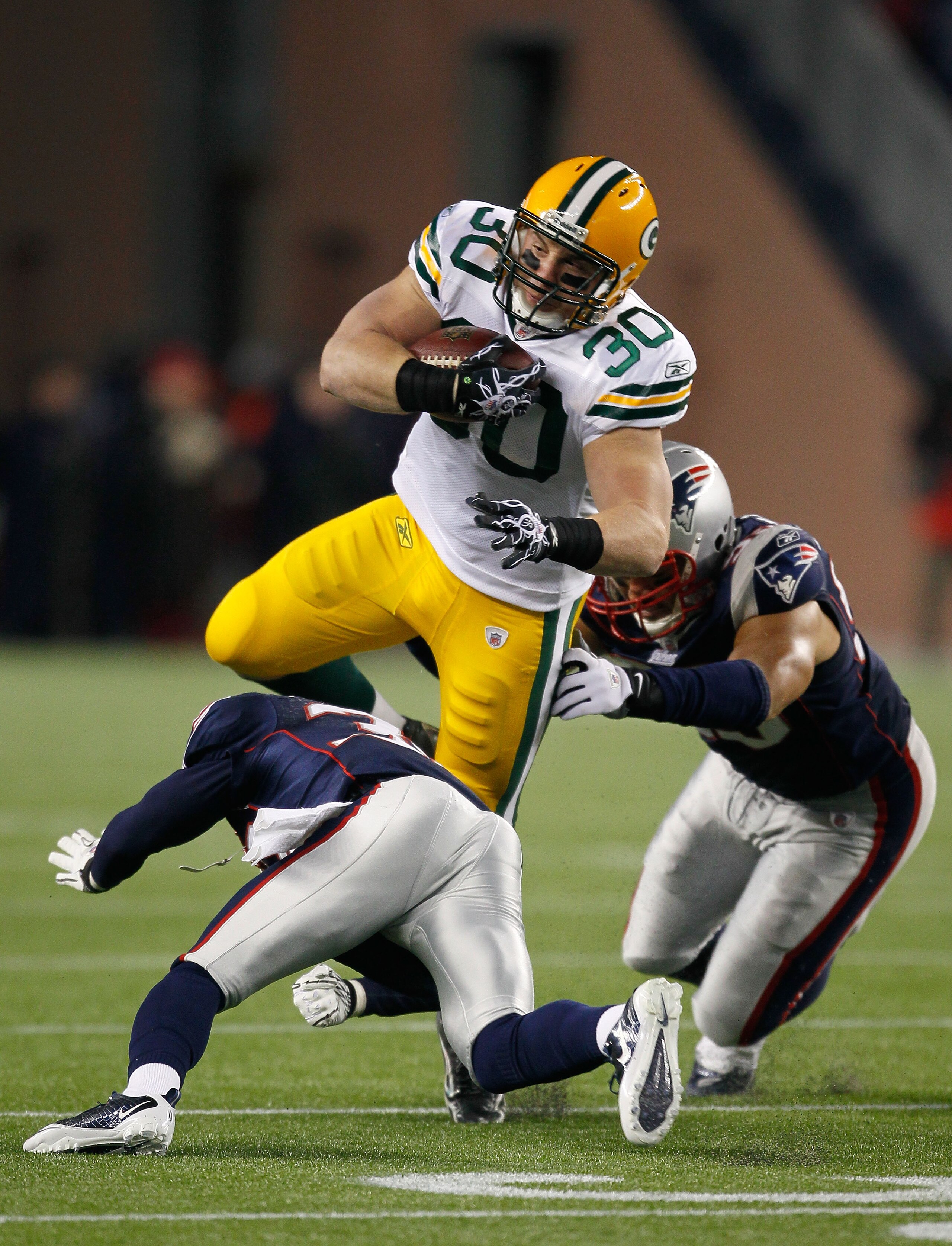FOXBORO, MA - DECEMBER 19:  Running back John Kuhn #30 of the Green Bay Packers is tackled by linebacker Tully Banta-Cain #95 and cornerback Devin McCourty #32 of the New England Patriots during the first quarter of the game at Gillette Stadium on Decembe