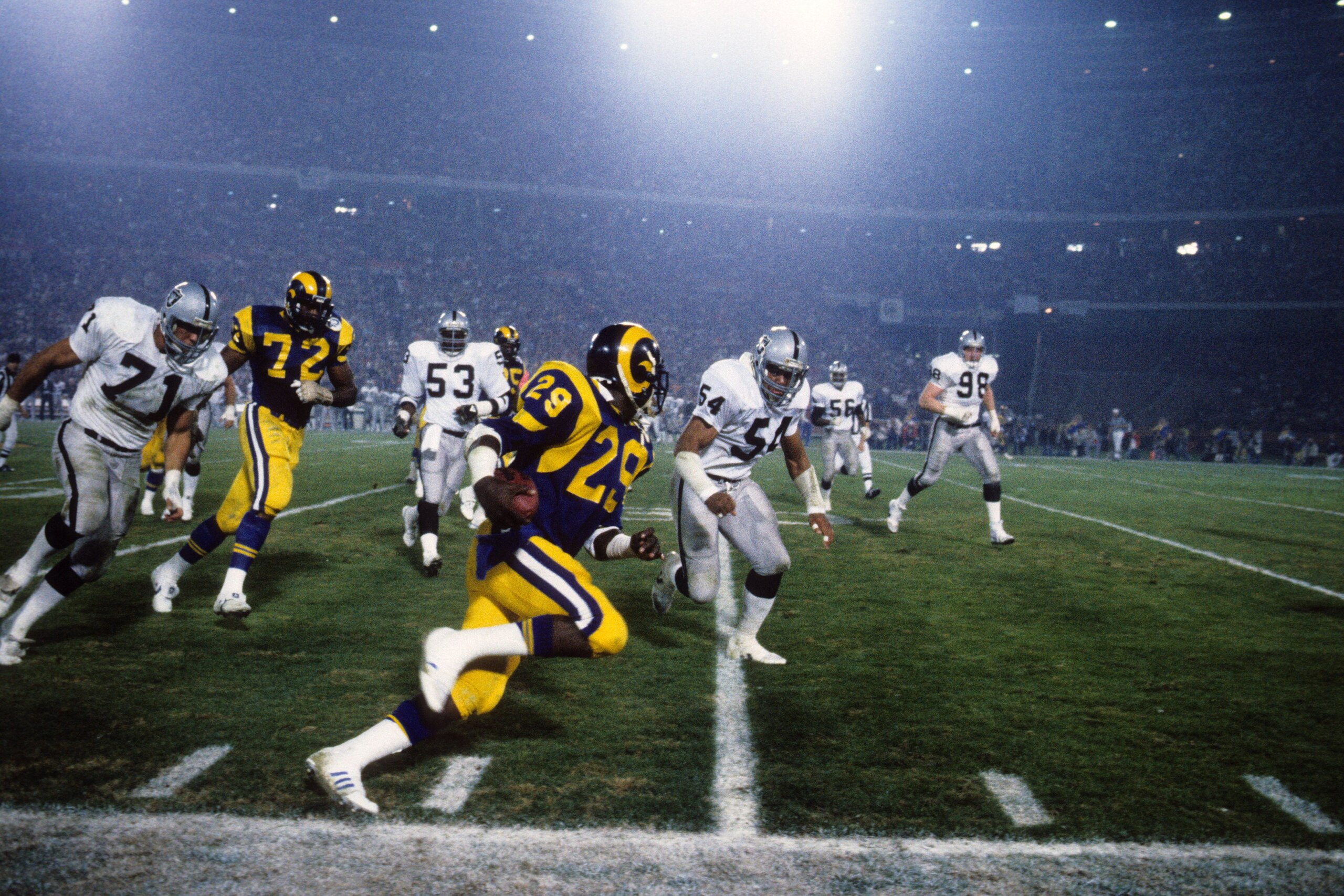 ANAHEIM, CA - DECEMBER 23:  Eric Dickerson #28 of the Los Angeles Rams runs for yards down the sideline against linebacker Reggie McKenzie #54 and Bill Pickel #71 of the Los Angeles Raiders during a game at Anaheim Stadium on December 23, 1985 in Anaheim,