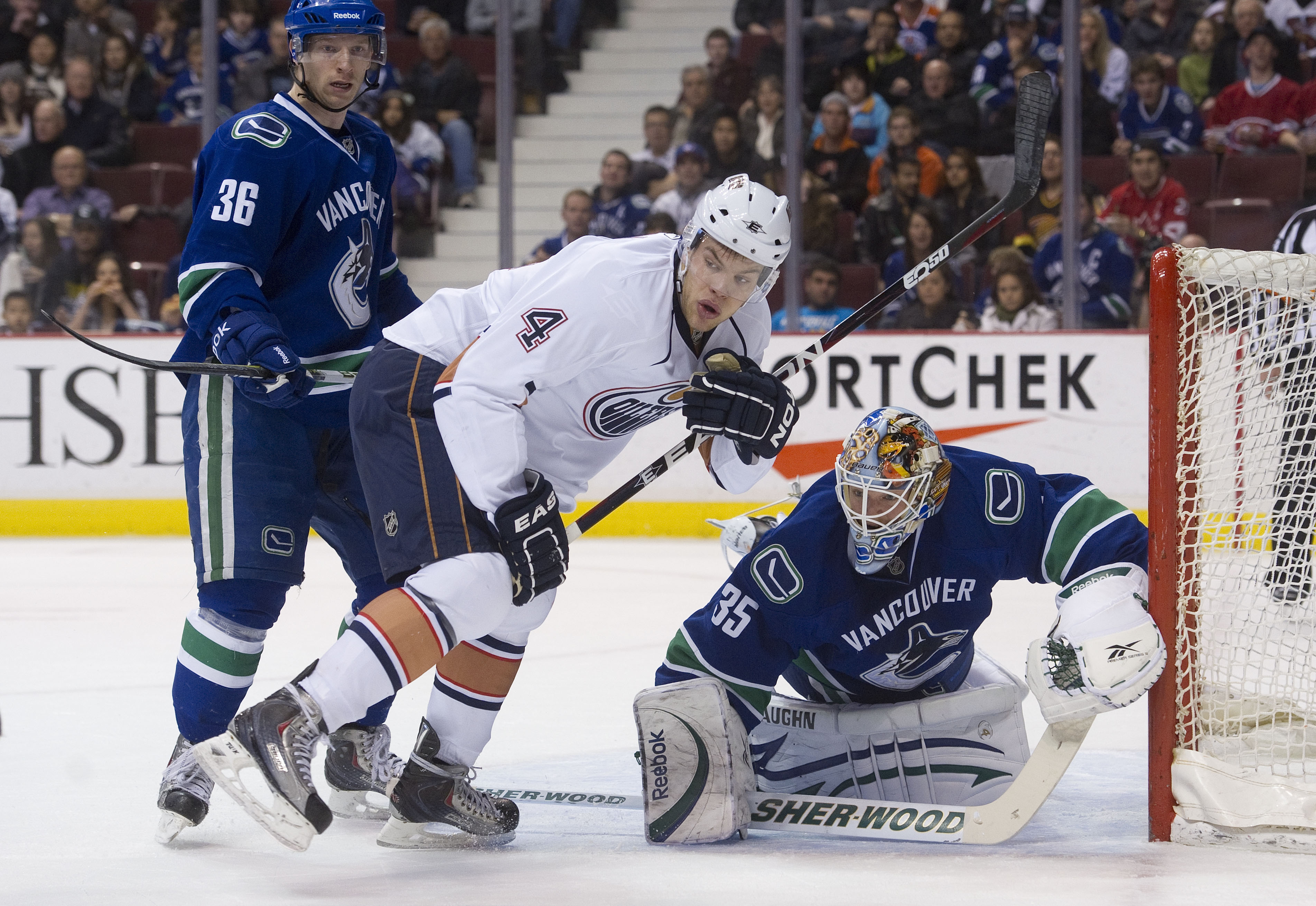 VANCOUVER, CANADA - DECEMBER 26: Taylor Hall #4 of the Edmonton Oilers along with goalie Cory Schneider #35 and Jannik Hansen #36 of the Vancouver Canucks watch the puck bounce into the corner during the first period in NHL action on December 26, 2010 at