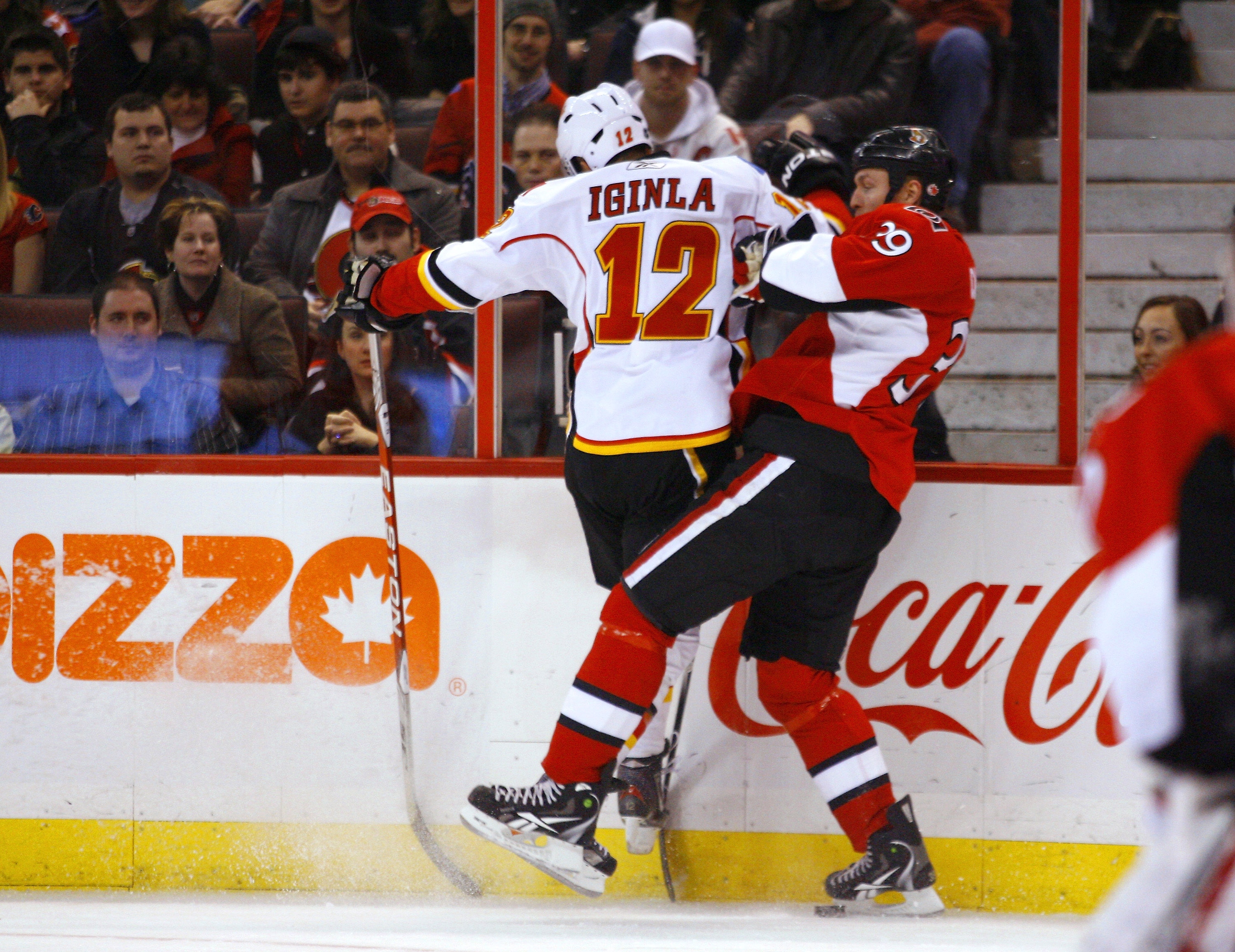OTTAWA, ON - JANUARY 14:  Jarome Iginla #12 of the Calgary Flames throws a big hit on Matt Carkner #39 of the Ottawa Senators along the far boards in a game at Scotiabank Place on January 14, 2011 in Ottawa, Canada.  (Photo by Phillip MacCallum/Getty Imag