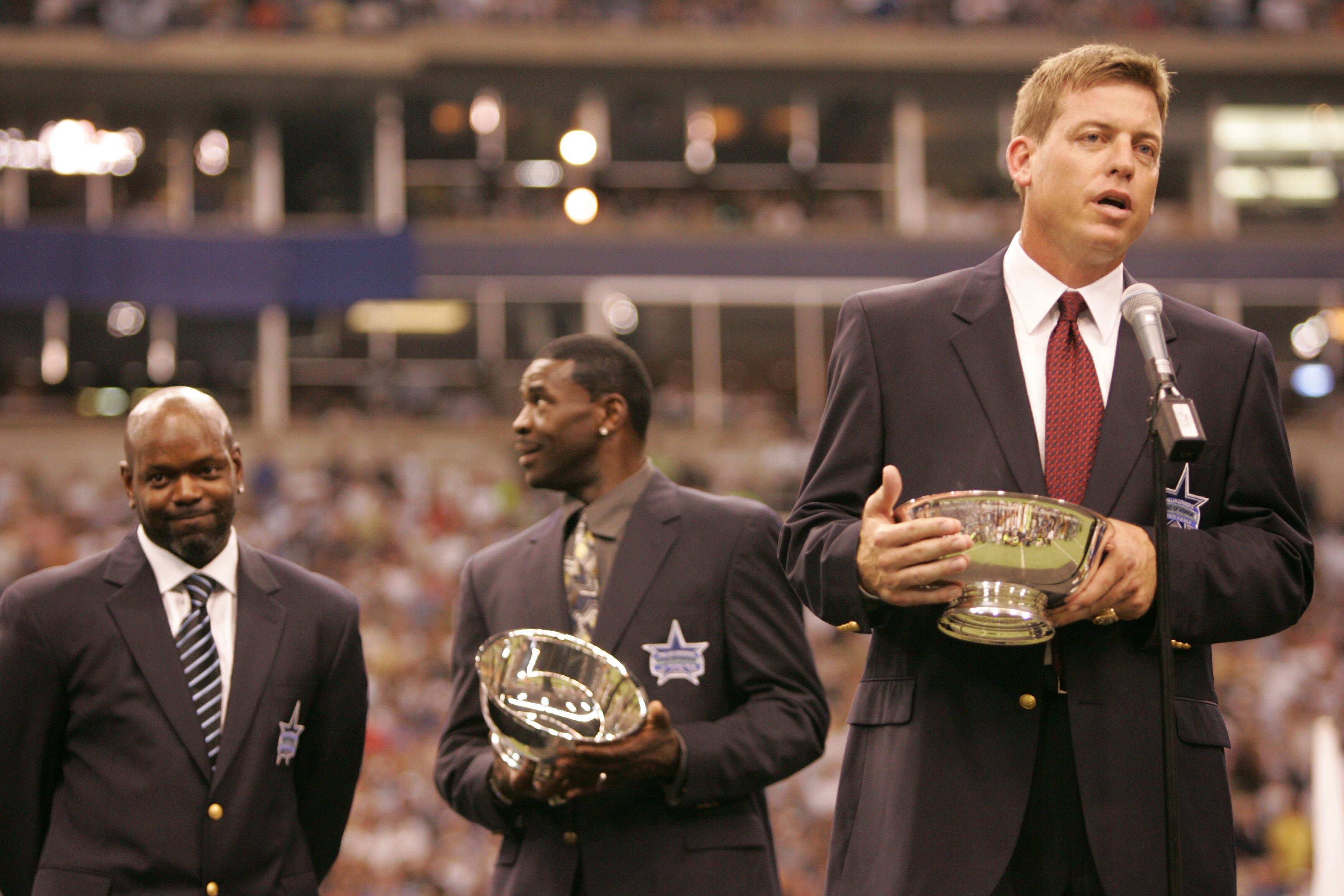 IRVING, TX - SEPTEMBER 19:  Troy Aikman, former Dallas Cowboys quaterback, speaks to the fans in front of former teammates Emmitt Smith (L) and Michael Irvin during a ceremony inducting Aikman into the Cowbos ring of honor at half-time of the game between