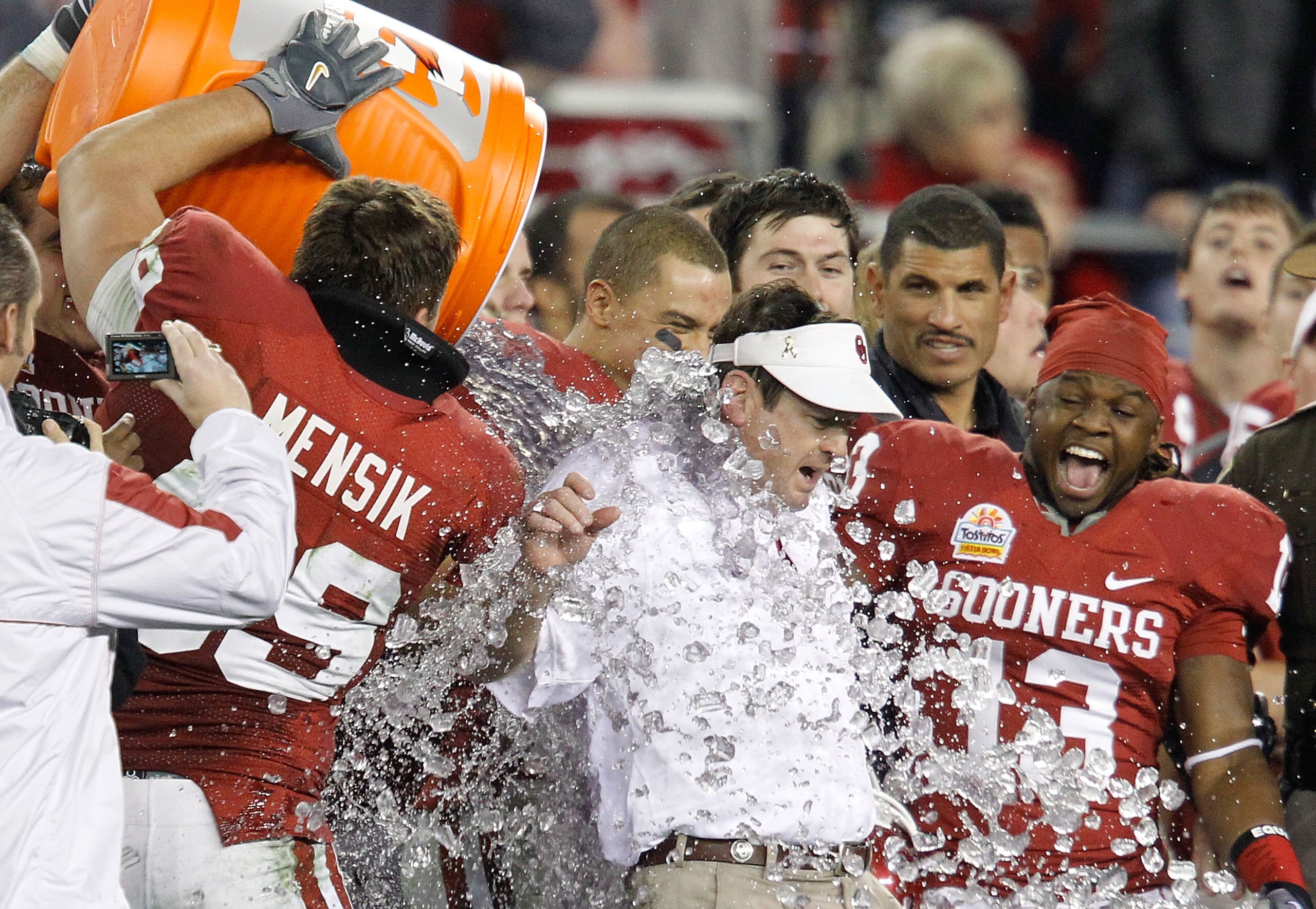 GLENDALE, AZ - JANUARY 01: Head coach Bob Stoops has a Gatorade bucket dumped on him by Eric Mensik #69 late in the fourth quarter before the Sooners 48-20 victory against the Connecticut Huskies during the Tostitos Fiesta Bowl at the Universtity of Phoe GLENDALE, AZ - JANUARY 01: Head coach Bob Stoops has a Gatorade bucket dumped on him by Eric Mensik #69 late in the fourth quarter before the Sooners 48-20 victory against the Connecticut Huskies during the Tostitos Fiesta Bowl at the Universtity of Phoe