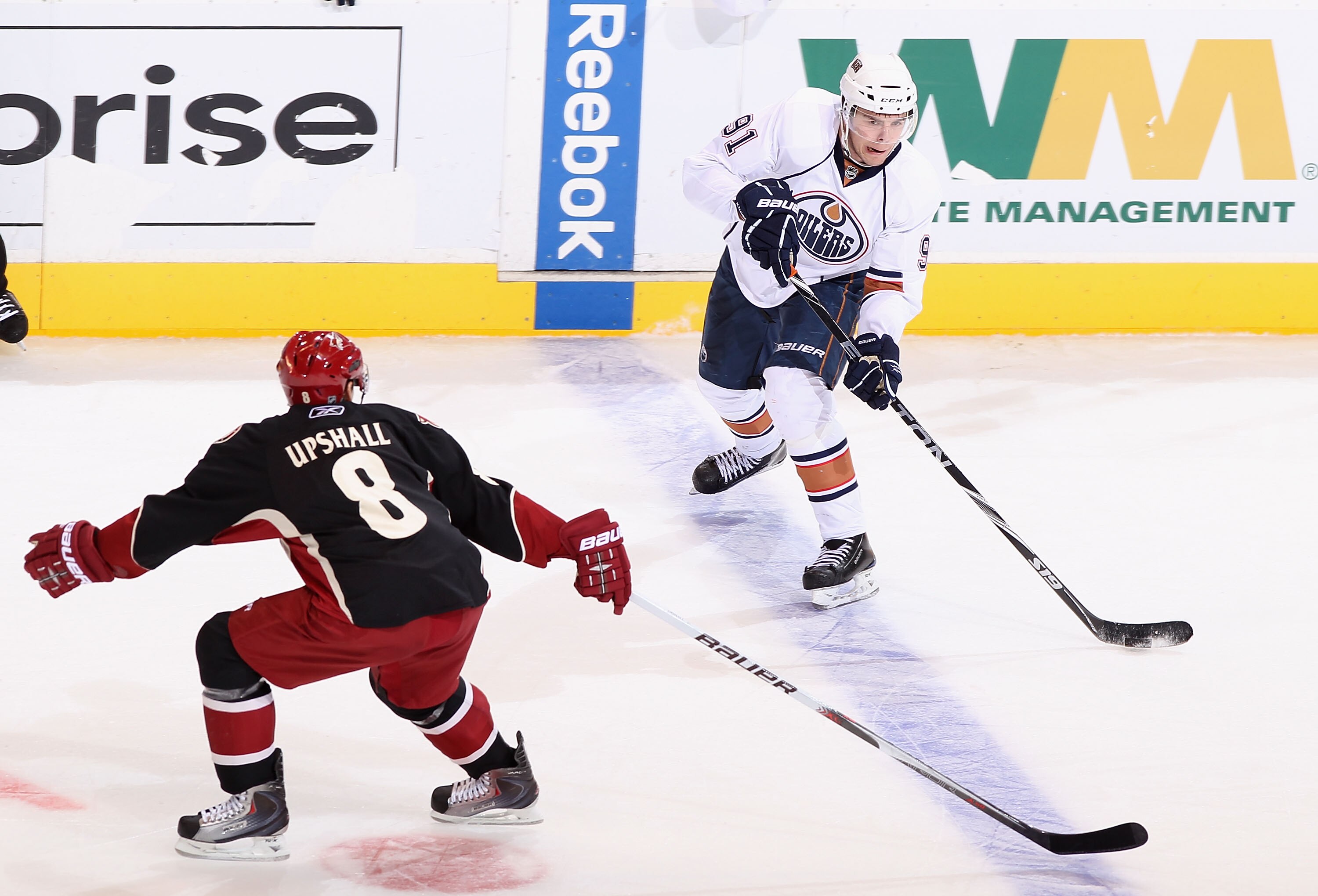 GLENDALE, AZ - JANUARY 25:  Magnus Paajarvi #91 of the Edmonton Oilers passes the puck under pressure from Scottie Upshall #8 of the Phoenix Coyotes during the NHL game at Jobing.com Arena on January 25, 2011 in Glendale, Arizona.  The Oilers defeated the