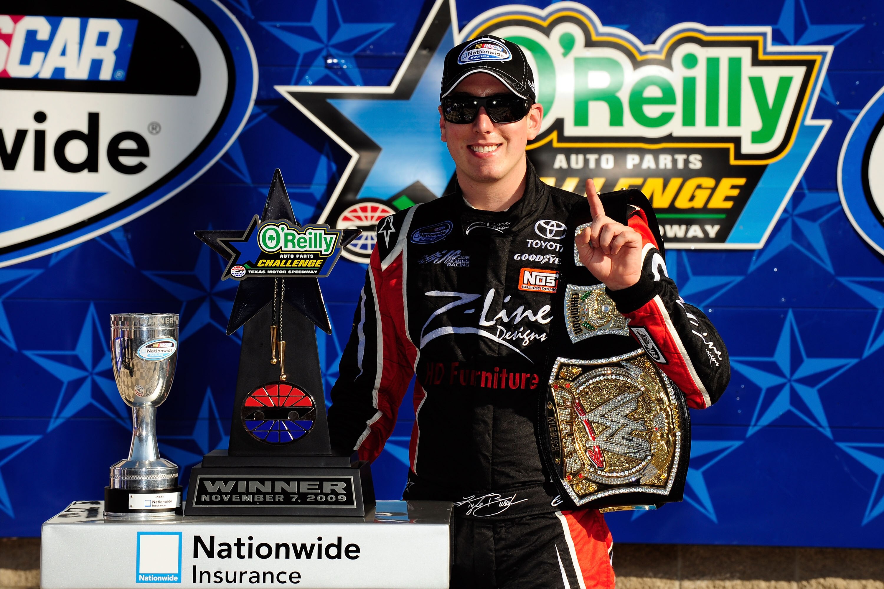 FORT WORTH, TX - NOVEMBER 07:  Kyle Busch, driver of the #18 Z-Line Designs/WWE Smackdown Toyota,  poses on victory lane with the trophy and a replica of the WWE world championship belt after winning the NASCAR Nationwide Series O'Reilly Challenge at Texa