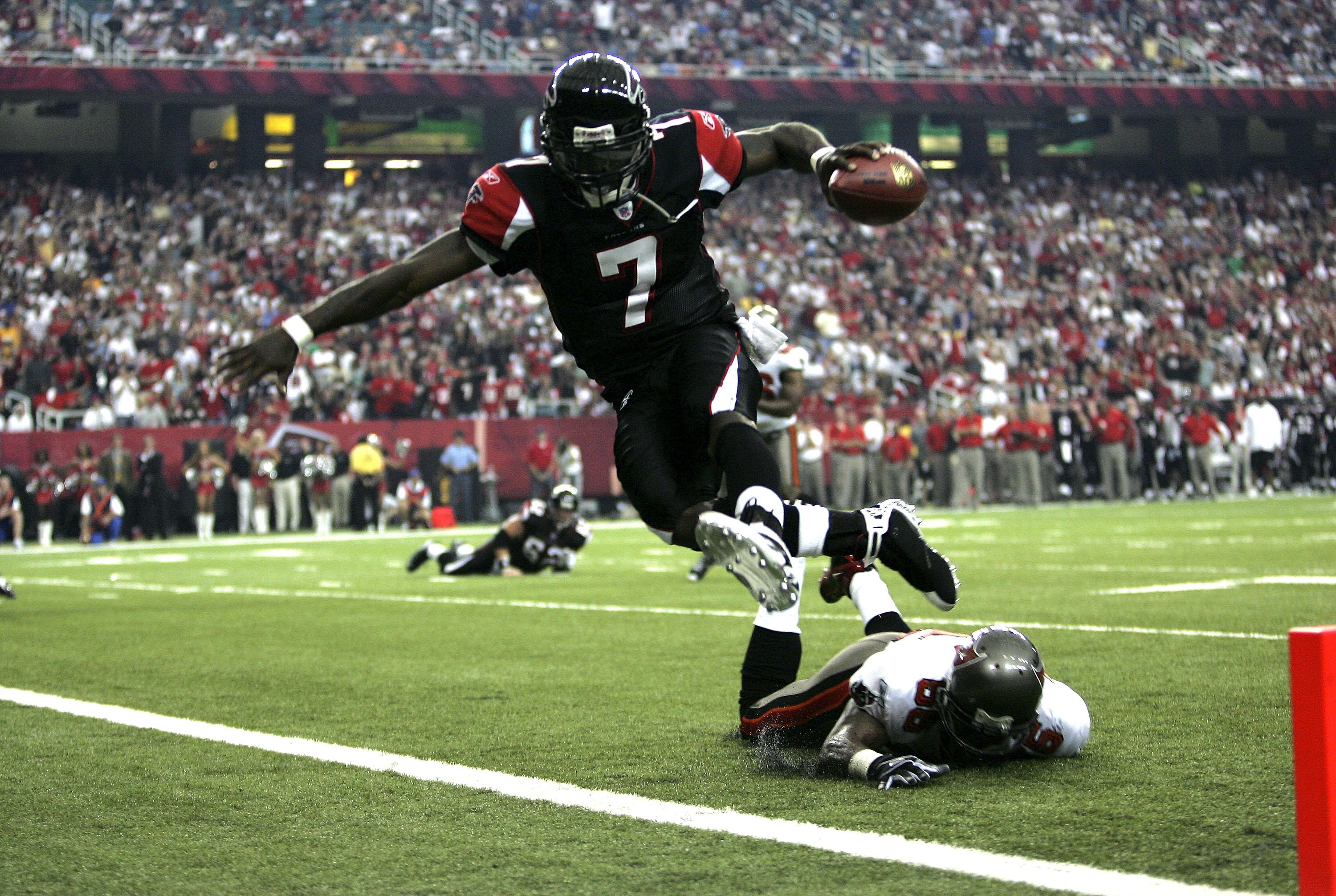 ATLANTA - SEPTEMBER 17:  Michael Vick #7 of the Atlanta Falcons jumps into the end zone as Ryan Nece #56 of the Tampa Bay Buccaneers falls during their game on September 17, 2006 at the Georgia Dome in Atlanta, Georgia.  (Photo By Streeter Lecka/Getty Ima