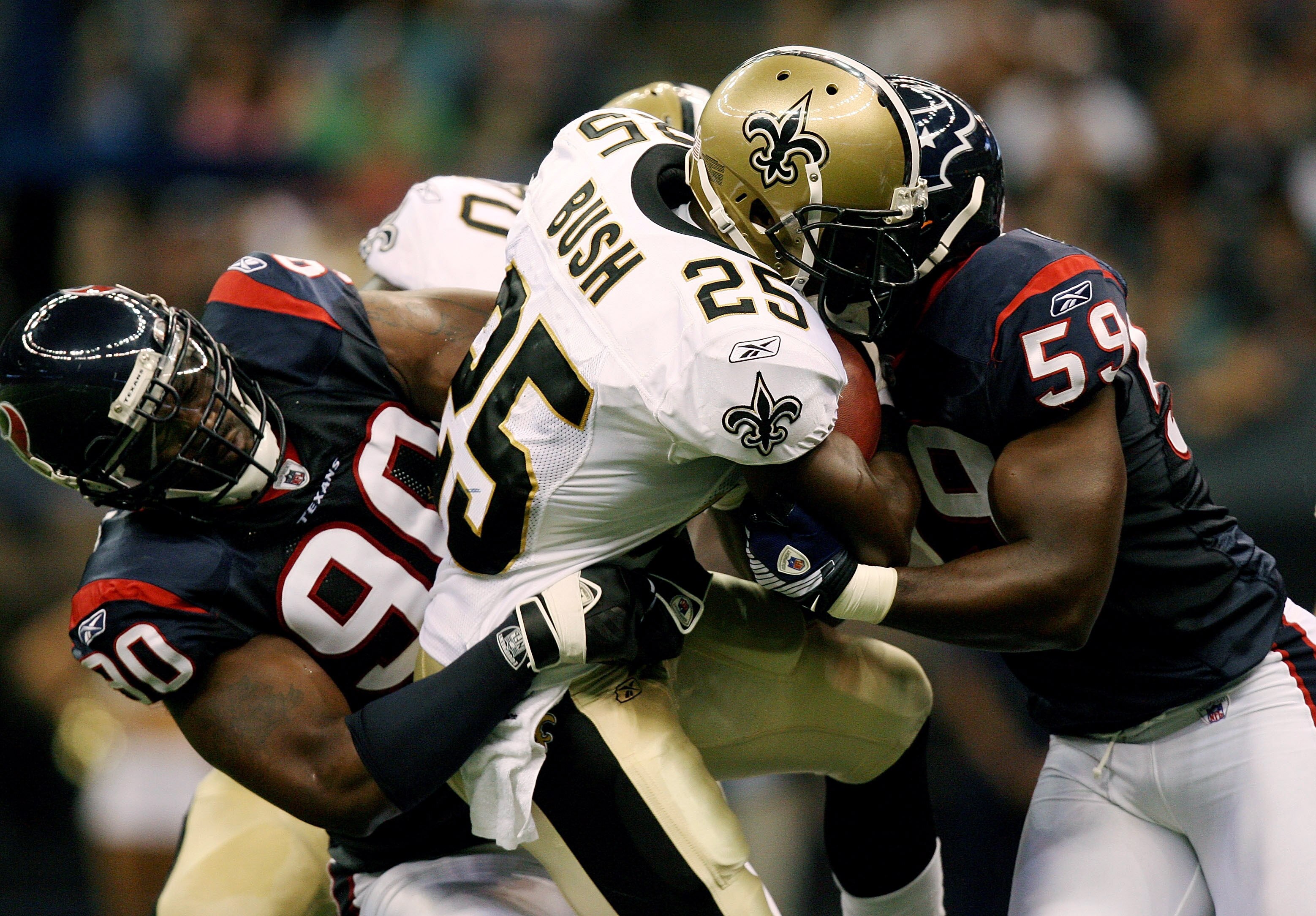 NEW ORLEANS - AUGUST 16:  Defensive end Mario Williams #90 and linebacker DeMeco Ryans #59 of the Houston Texans brings down running back Reggie Bush #25 of the New Orleans Saints during a pre-season game at Louisiana Superdome on August 16, 2008 in New O