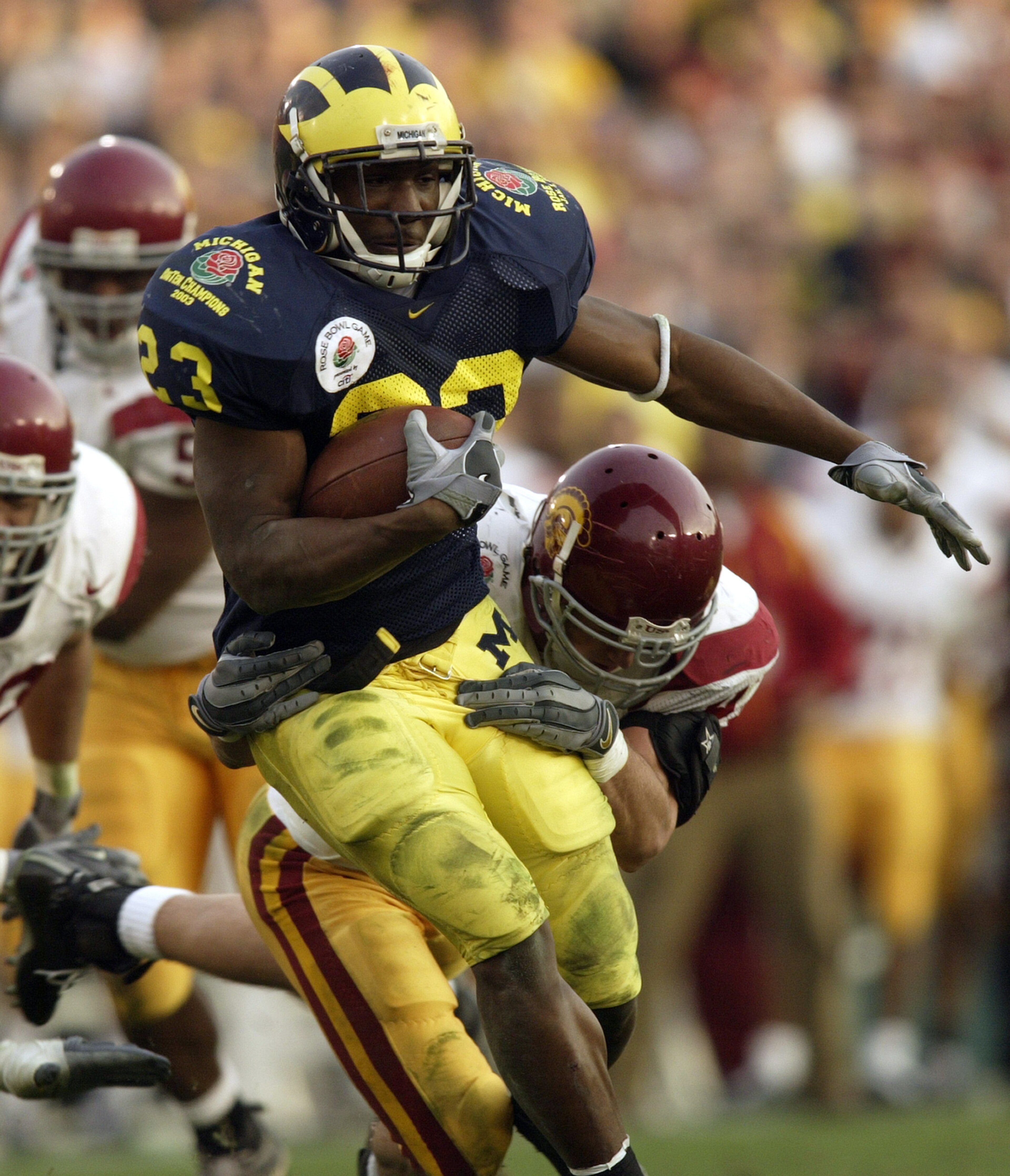 PASADENA, CA - JANUARY 1:  Running back Chris Perry #23 of the Michigan Wolverines attempts to break loose from the grasp of a USC Trojans defender during the 2004 Rose Bowl game on January 1, 2004 at the Rose Bowl in Pasadena, California. USC defeated Mi