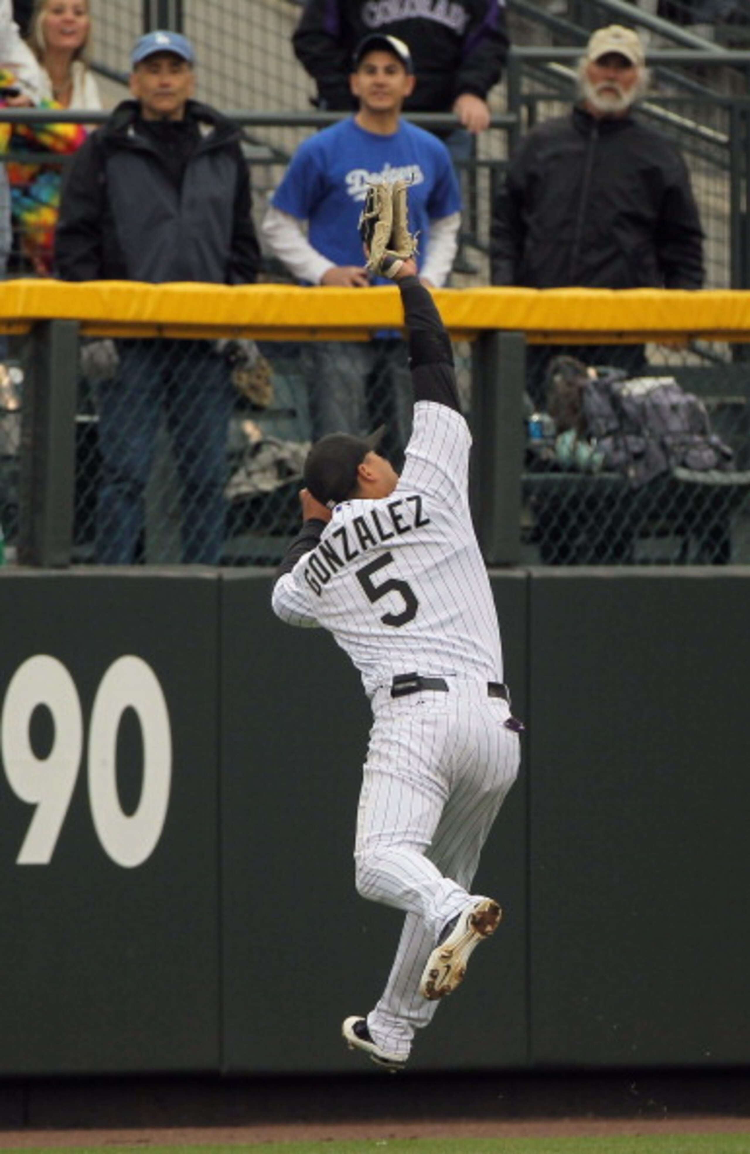 DENVER, CO - APRIL 06:  Leftfielder Carlos Gonzalez #5 of the Colorado Rockies leaps as he nears the wall to catch a fly ball by Rafael Furcal #15 of the Los Angeles Dodgers for the first out of the ninth inning at Coors Field on April 6, 2011 in Denver,