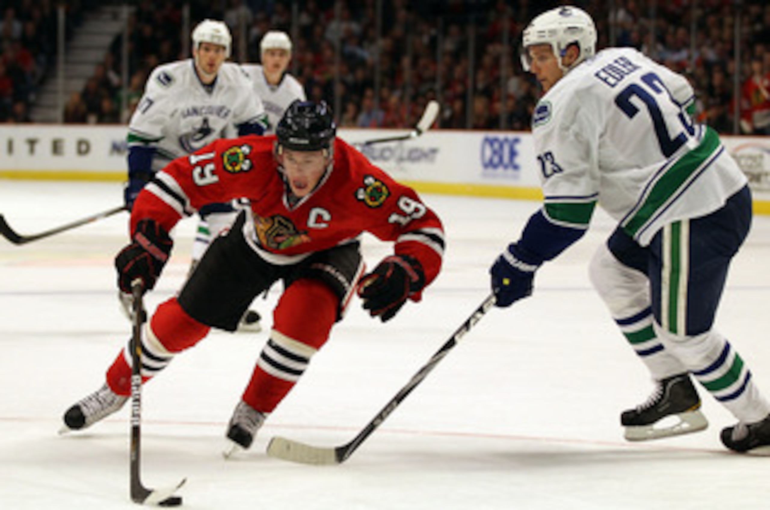 CHICAGO, IL - DECEMBER 03: Jonathan Toews #19 of the Chicago Blackhawks controls the puck against Alexander Edler #23 of the Vancouver Canucks at the United Center on December 3, 2010 in Chicago, Illinois. The Canucks defeated the Blackhawks 3-0.  (Photo