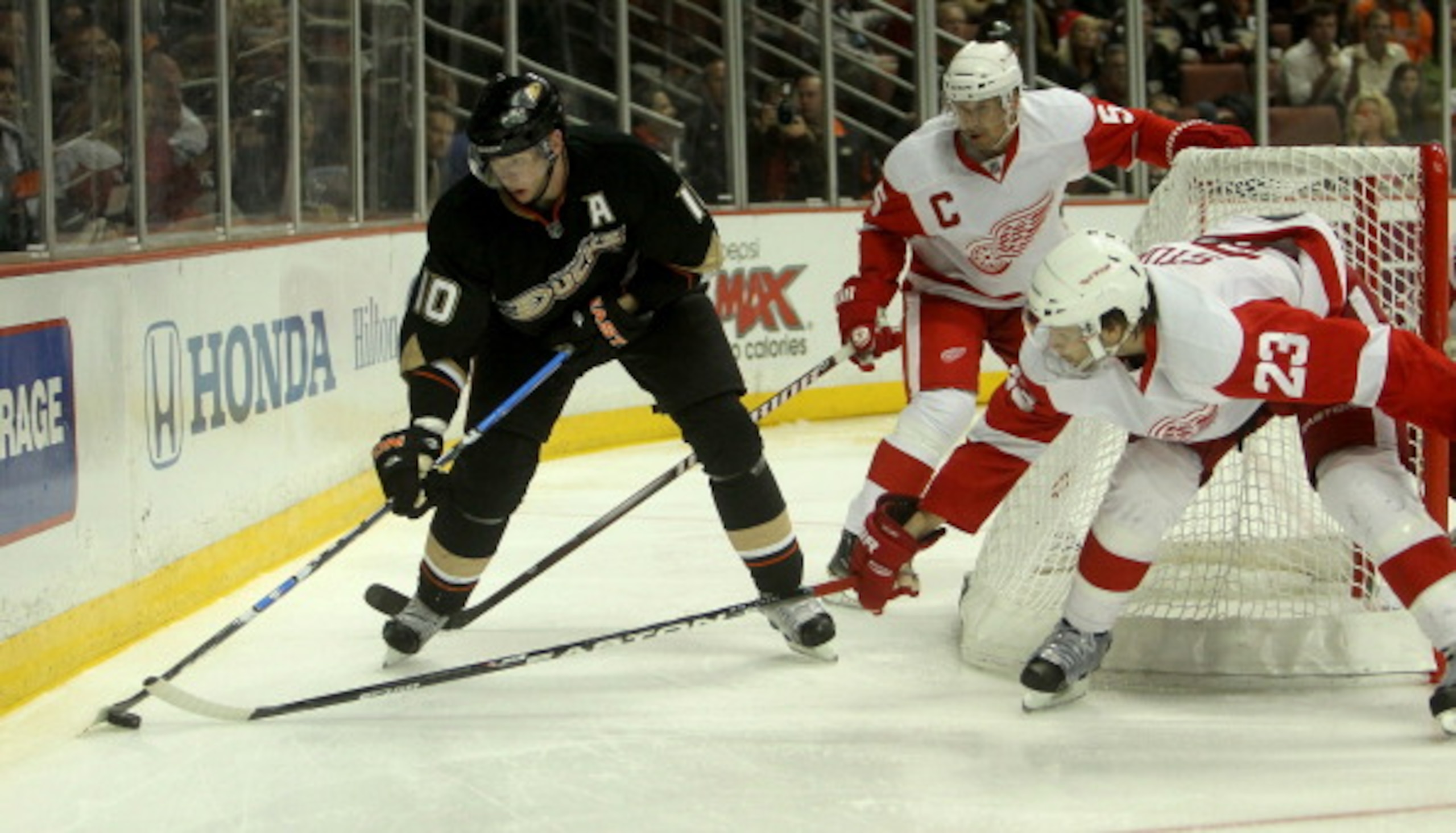 ANAHEIM, CA - MARCH 2:   Corey Perry #10 of the Anaheim Ducks plays the puck behind the net as Brad Stuart #23 and Nicklas Lidstrom #5 of the Detroit Red Wings defend on March 2, 2011 at the Honda Center in Anaheim, California.   The Ducks won 2-1 in over