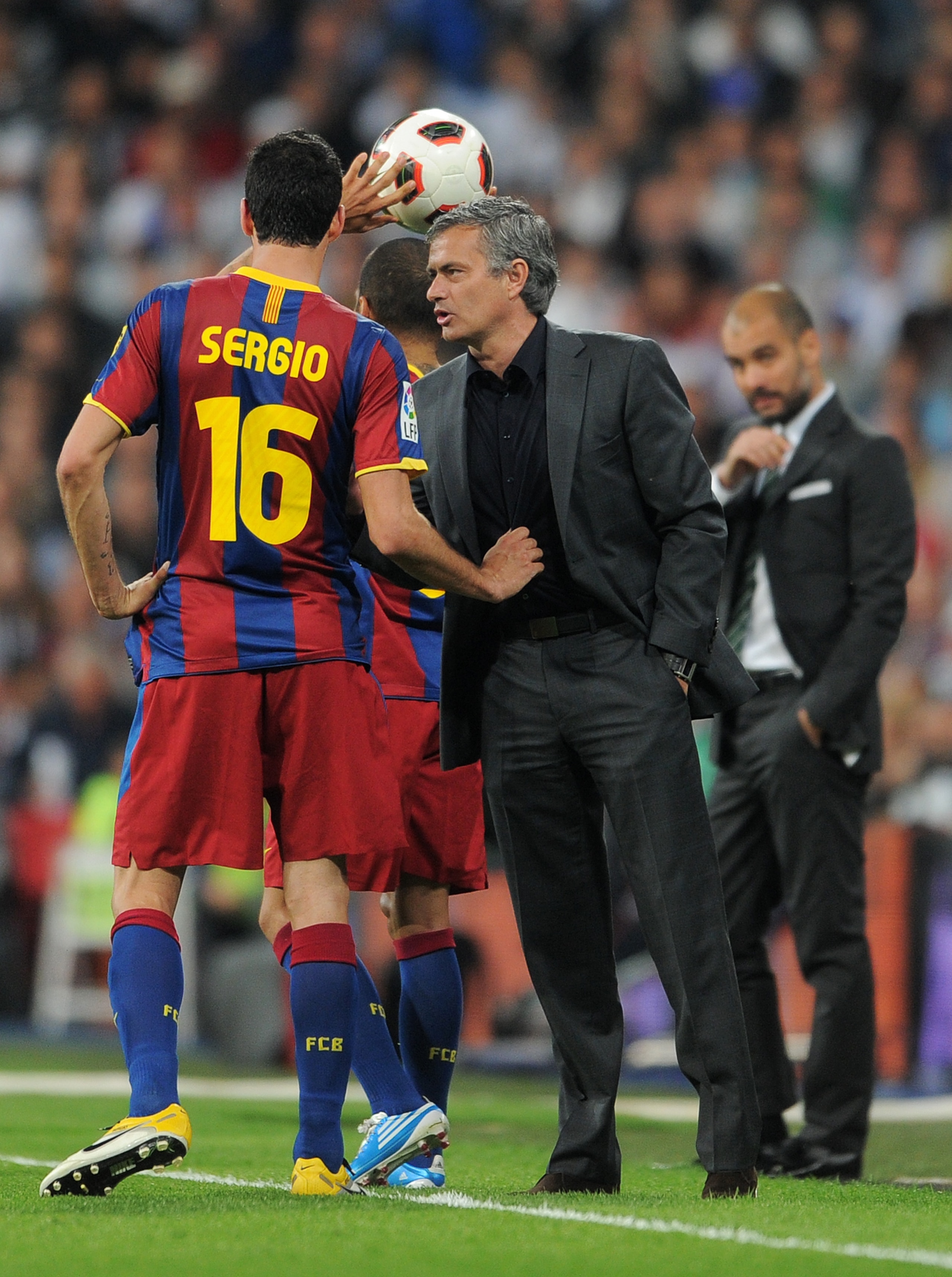 MADRID, SPAIN - APRIL 16:  Sergio Busquets (L) of Barcelona holds head coach Jose Mourinho (R) of Real Madrid by his shirt as they chat while head coach Josep Guardiola of Barcelona looks on in the background during the la Liga match between Real Madrid a