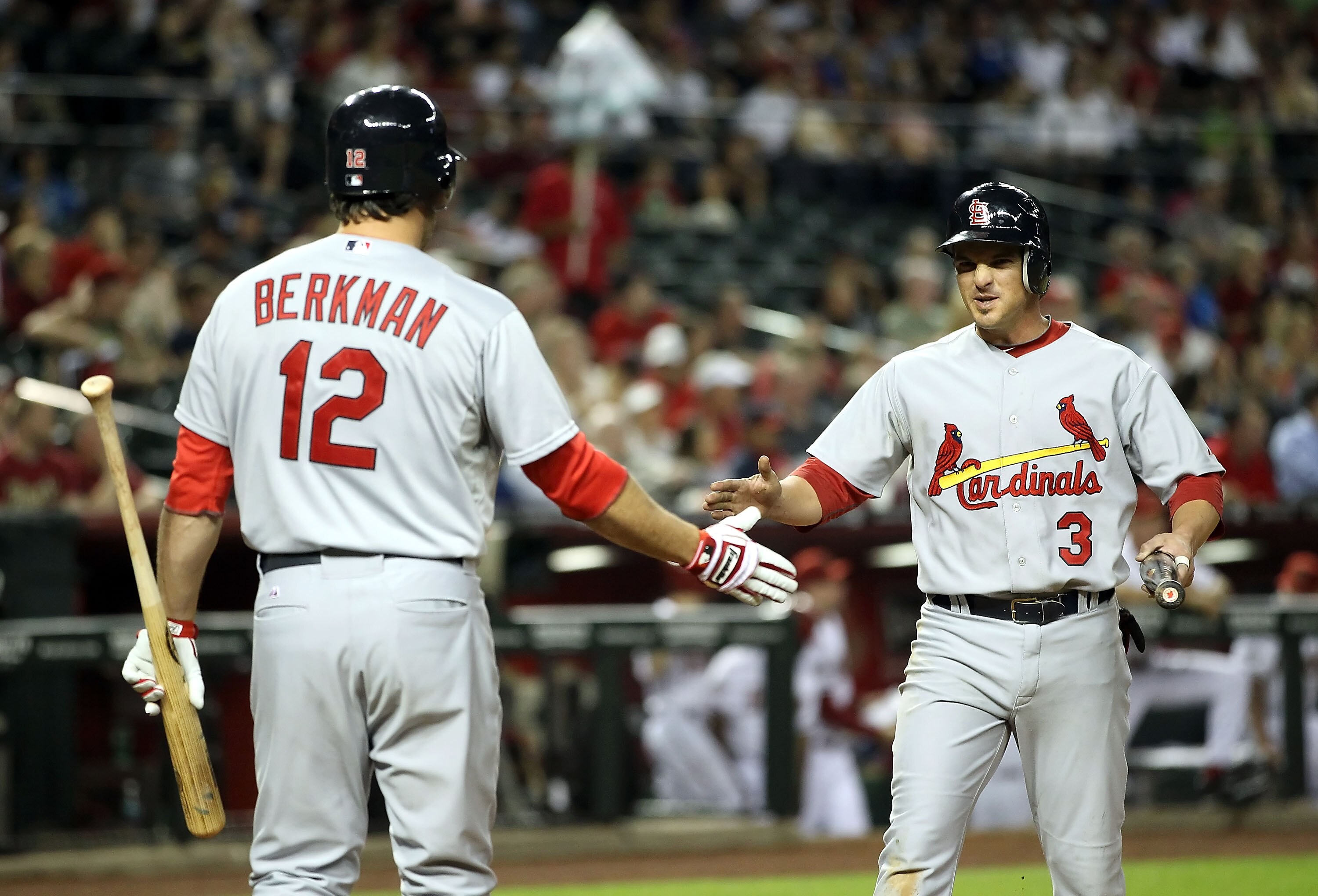 PHOENIX, AZ - APRIL 12:  Ryan Theriot #3 of the St. Louis Cardinals high fives teammate Lance Berkman #12 after scoring a fifth inning run against the Arizona Diamondbacks during the Major League Baseball game at Chase Field on April 12, 2011 in Phoenix,