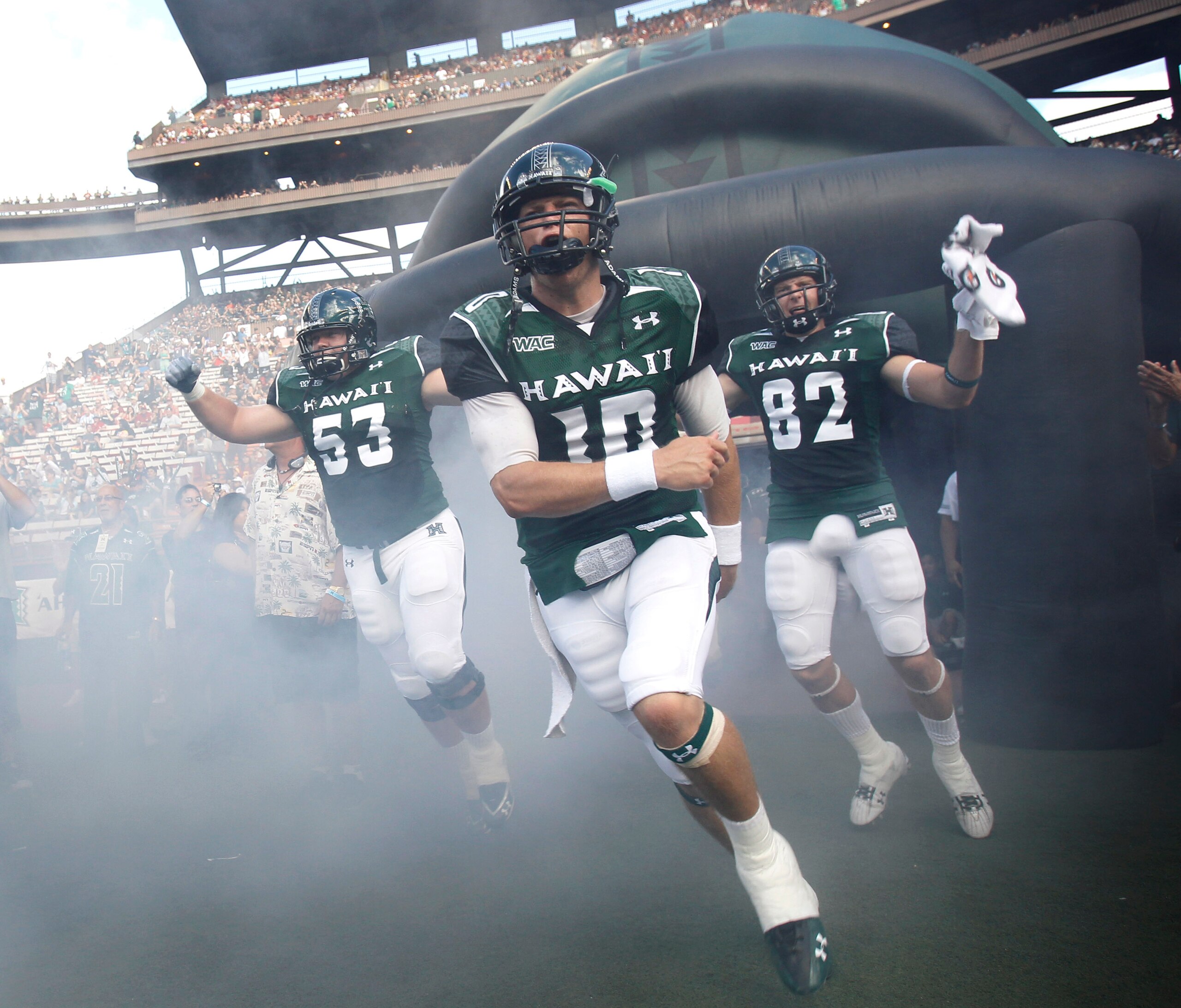 HONOLULU - SEPTEMBER 02: Levi Legay #53, Shane Austin #10, and Jett Jasper #82 of the University of Hawaii Warriors and other team members rush out of the tunnel to take the field in their season opener against the University of Southern California Trojan
