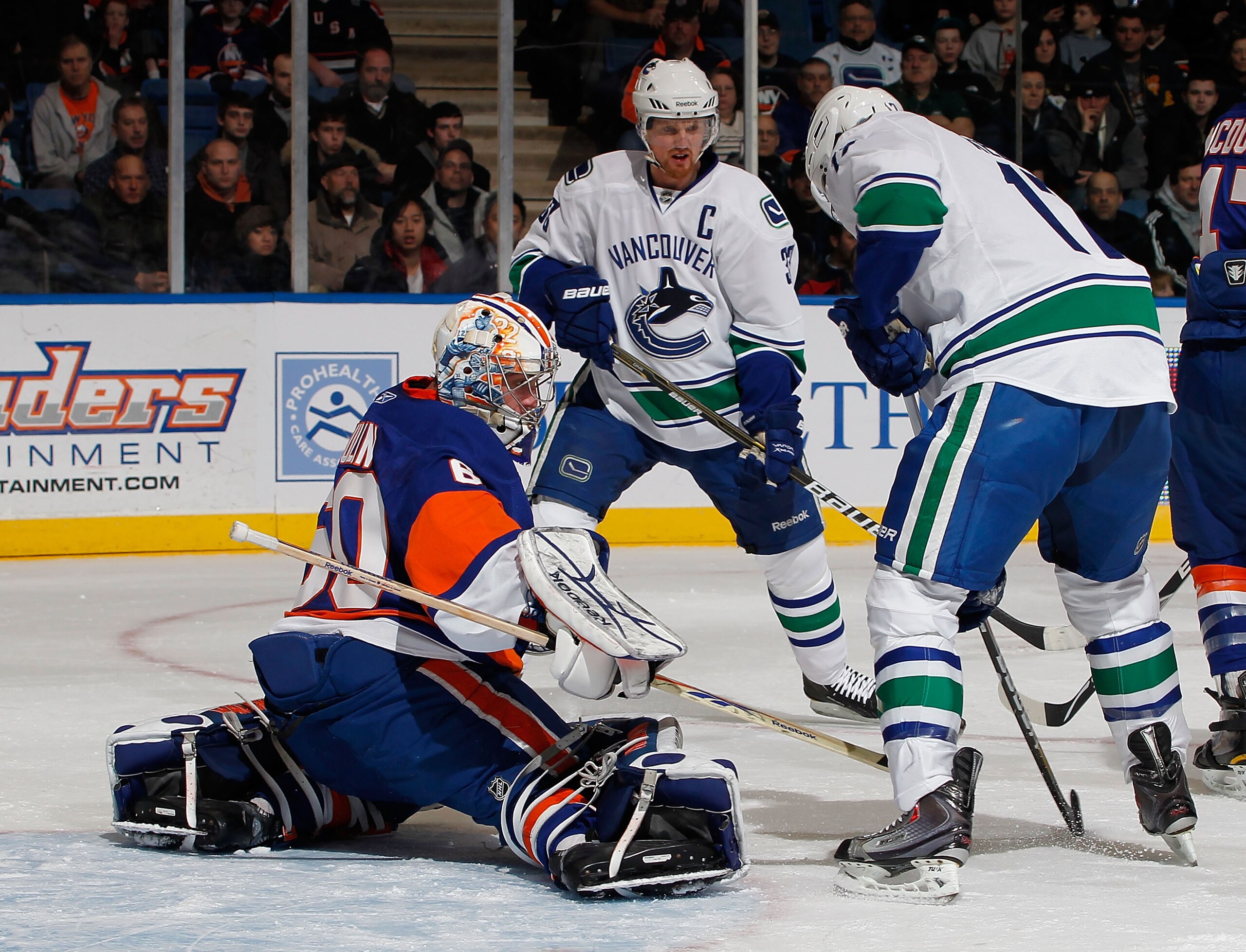 UNIONDALE, NY - JANUARY 11:  Goalie Kevin Poulin #60 of the New York Islanders makes a save on a shot by Ryan Kesler #17 of the Vancouver Canucks as Henrik Sedin #33 of the Canucks looks on during the first period of an NHL hockey game at Nassau Coliseum 