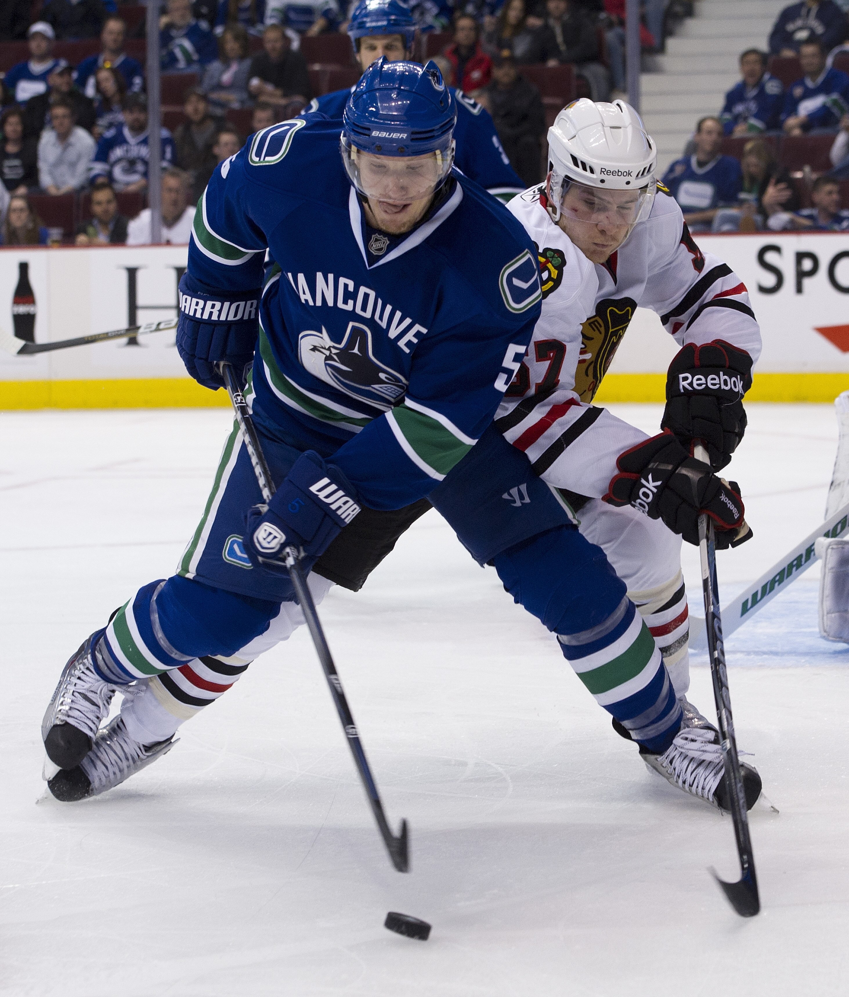 VANCOUVER, CANADA - APRIL 21: Christian Ehrhoff #5 of the Vancouver Canucks tries to clear the puck before getting checked by Ben Smith #57 of the Chicago Blackhawks during the third period in Game Five of the Western Conference Quarterfinals during the 2
