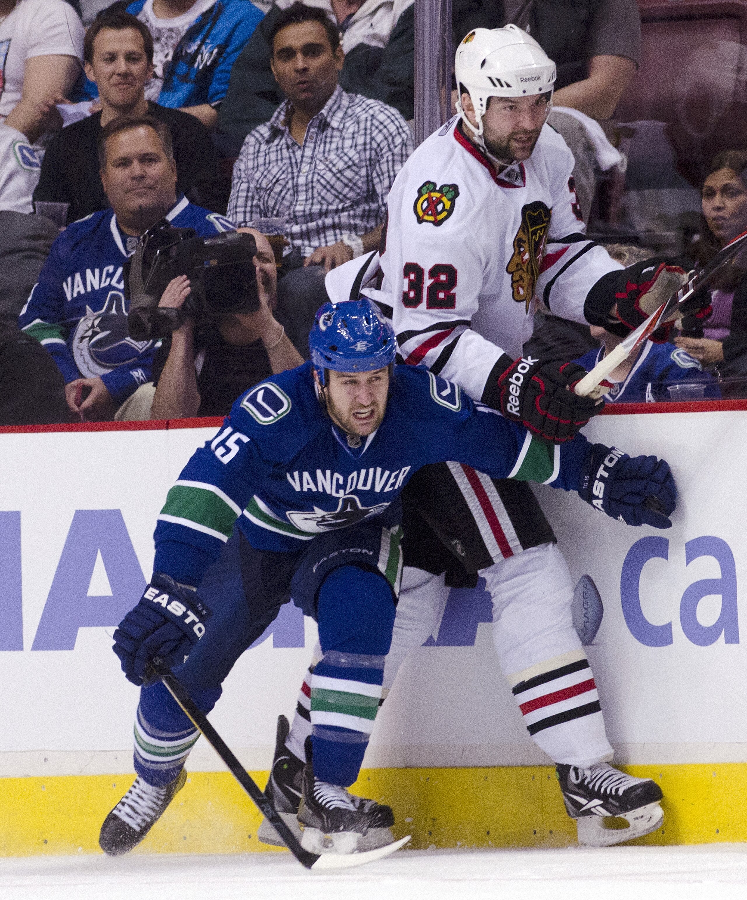 VANCOUVER, CANADA - APRIL 21: Tanner Glass #15 of the Vancouver Canucks hits John Scott #32 of the Chicago Blackhawks along the side boards during the third period in Game Five of the Western Conference Quarterfinals during the 2011 NHL Stanley Cup Playof