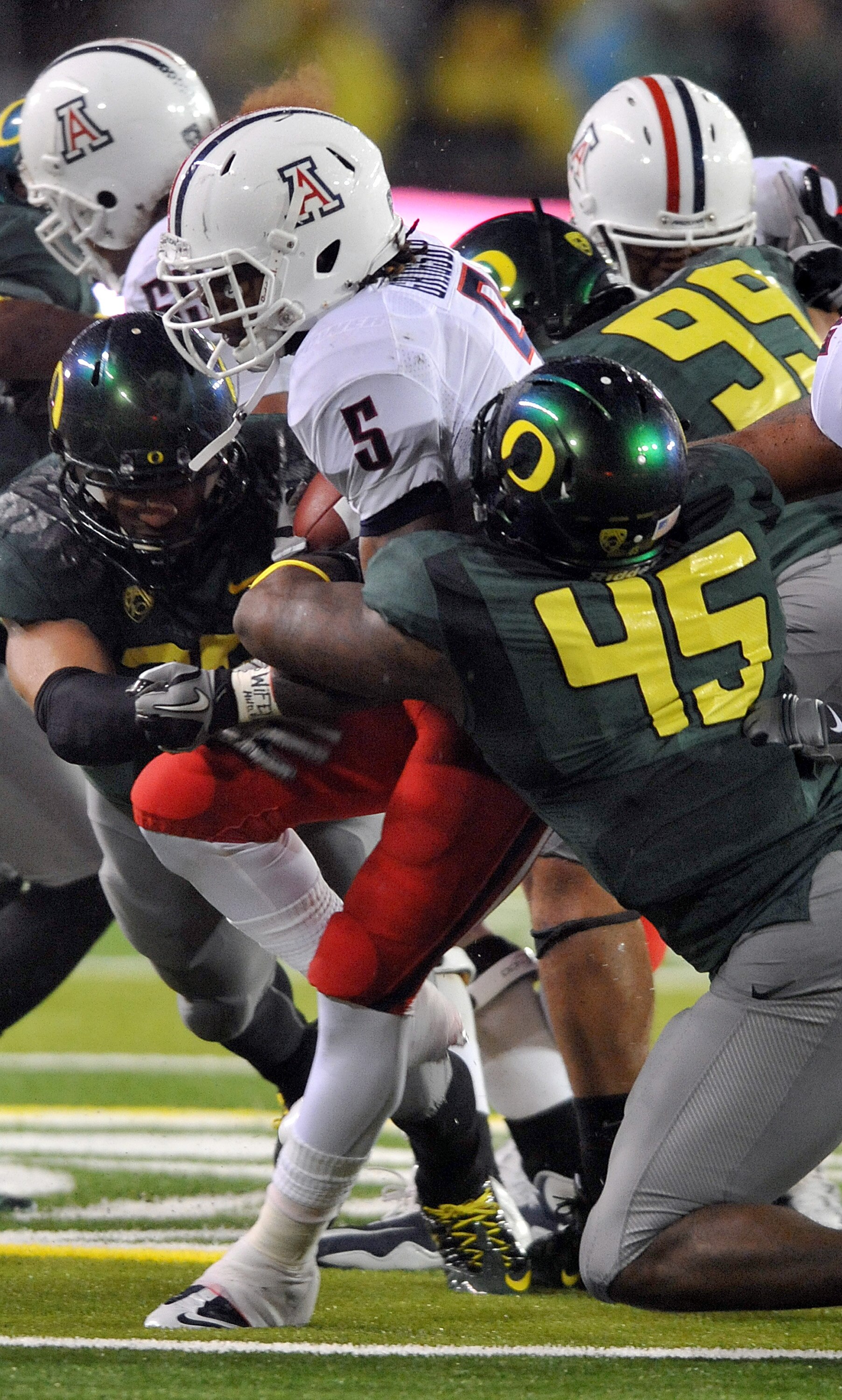 EUGENE, OR - NOVEMBER 26: Running back Nic Grigsby #5 of the Arizona Wildcats is tackled by defensive end Terrell Turner #45 and defensive tackle Zac Clark #99 of the Oregon Ducks in the fourth quarter of the game at Autzen Stadium on November 26, 2010 in