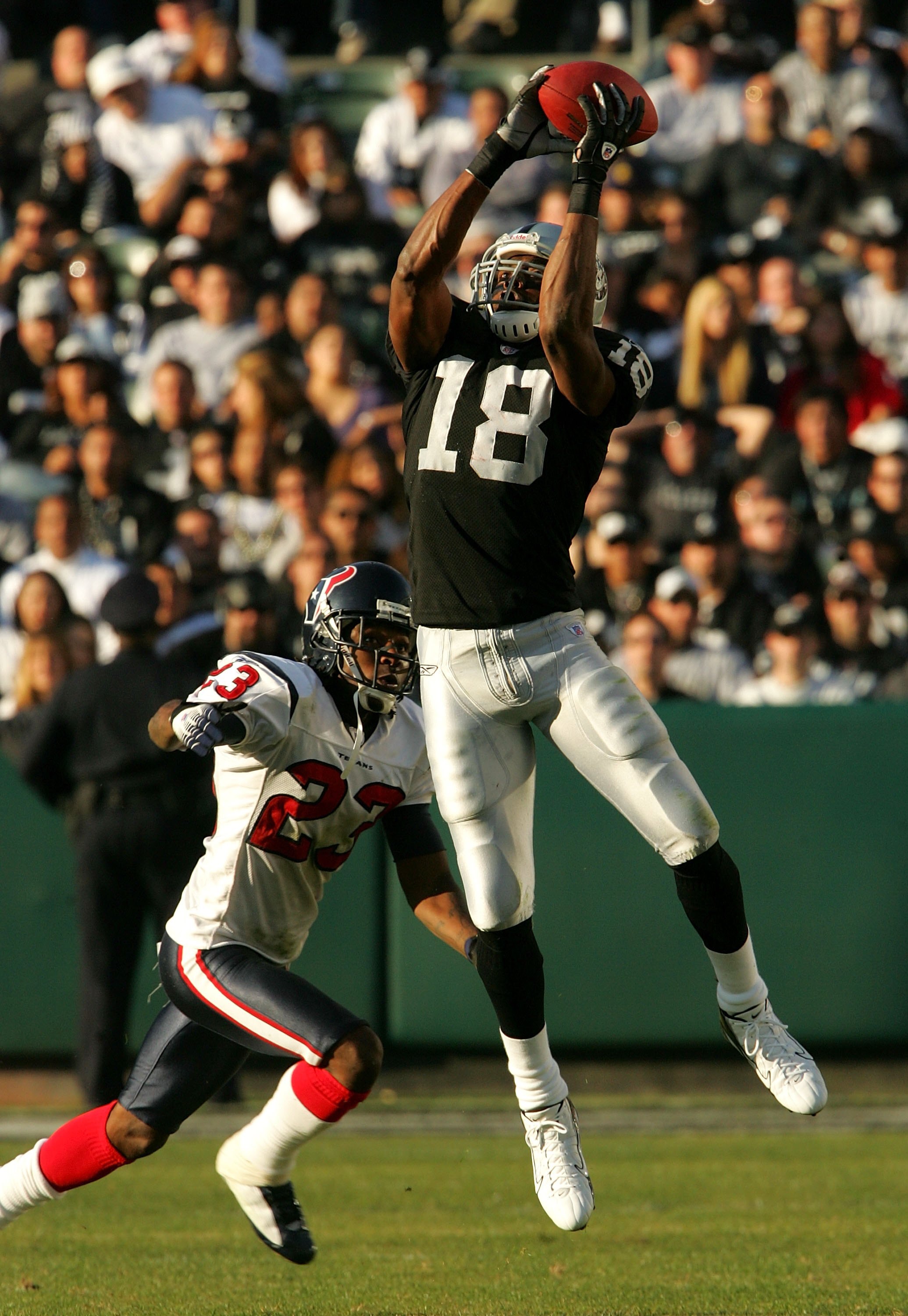 OAKLAND, CA - DECEMBER 3:  Randy Moss #18 of the Oakland Raiders leaps to make a catch in front of Dunta Robinson #23 of the Houston Texans at McAfee Coliseum December 3, 2006 in Oakland, California. Houston won 23-17.  (Photo by Stephen Dunn/Getty Images