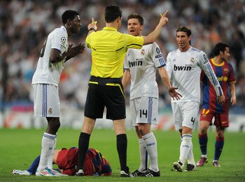 MADRID, SPAIN - APRIL 27:  Emmanuel Adebayor (L) and Xabi Alonso (R) of Real Madrid argue with referee Wolfgang Stark (C) as Daniel Alves of Barcelona lays on the pitch and Sergio Ramos looks on during the UEFA Champions League Semi Final first leg match