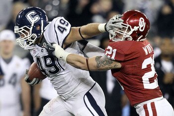 GLENDALE, AZ - JANUARY 01:  Anthony Sherman #49 of the Connecticut Huskies stiff arms Tom Wort #21 of the Oklahoma Sooners in the fourth quarter during the Tostitos Fiesta Bowl at the Universtity of Phoenix Stadium on January 1, 2011 in Glendale, Arizona.