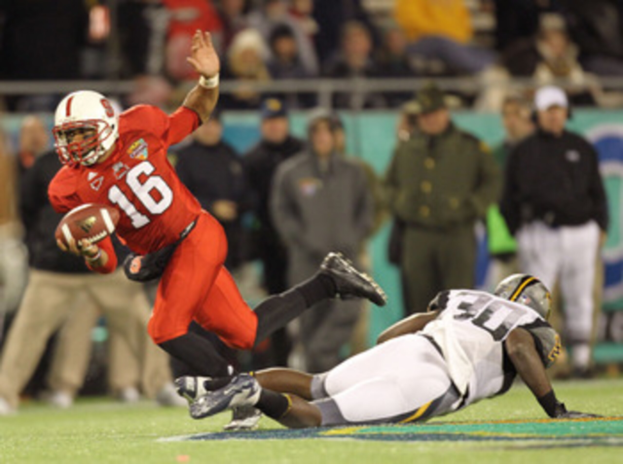 ORLANDO, FL - DECEMBER 28:  Russell Wilson #16 of the North Carolina State Wolfpack scrambles to get away from J.T. Thomas #30 of the West Virginia Mountineers during the Champs Sports Bowl at Florida Citrus Bowl Stadium on December 28, 2010 in Orlando, F
