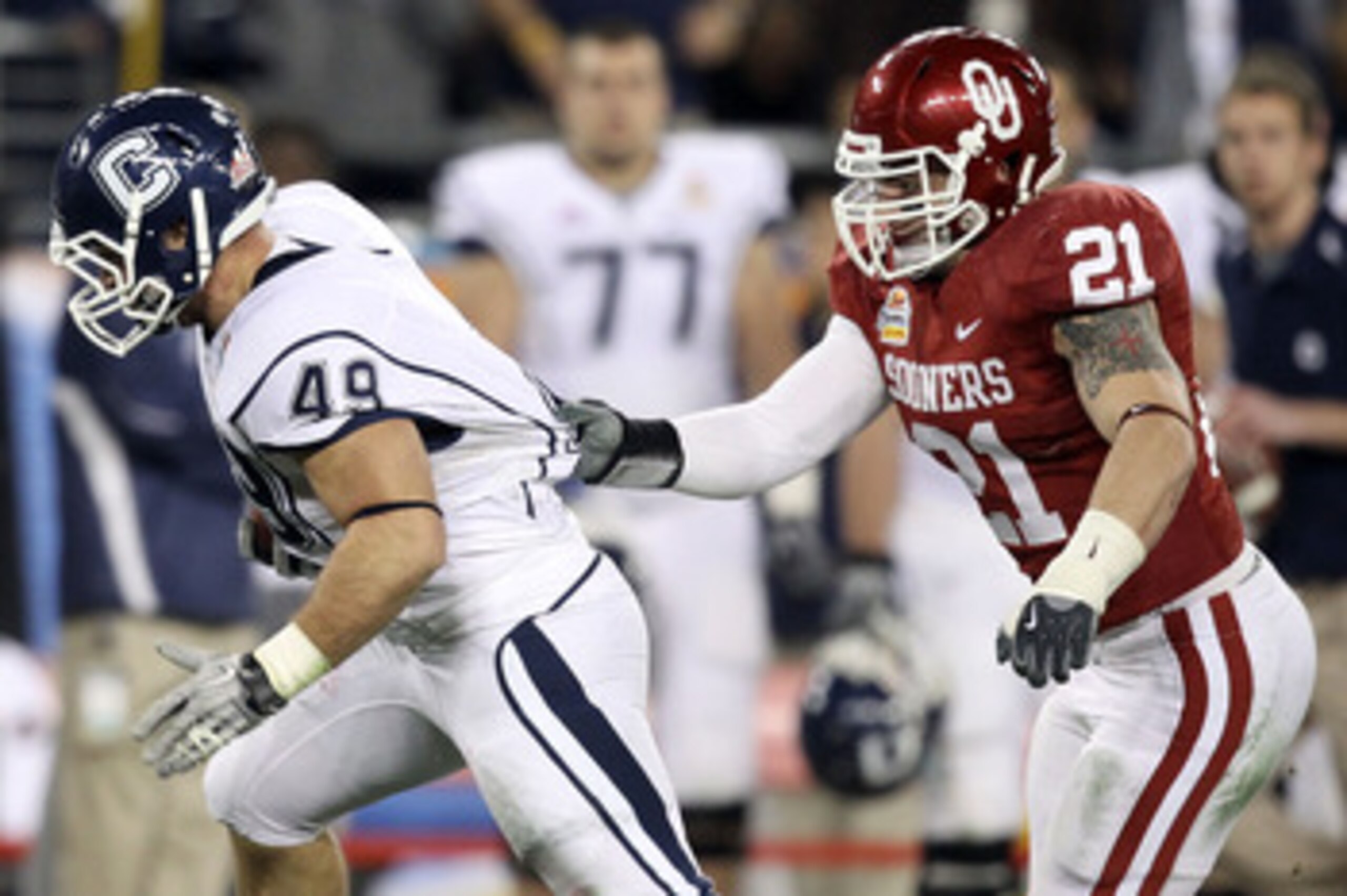 GLENDALE, AZ - JANUARY 01:  Anthony Sherman #49 of the Connecticut Huskies runs the ball as his jersey is grabbed by Tom Wort #21 of the Oklahoma Sooners in the fourth quarter during the Tostitos Fiesta Bowl at the Universtity of Phoenix Stadium on Januar