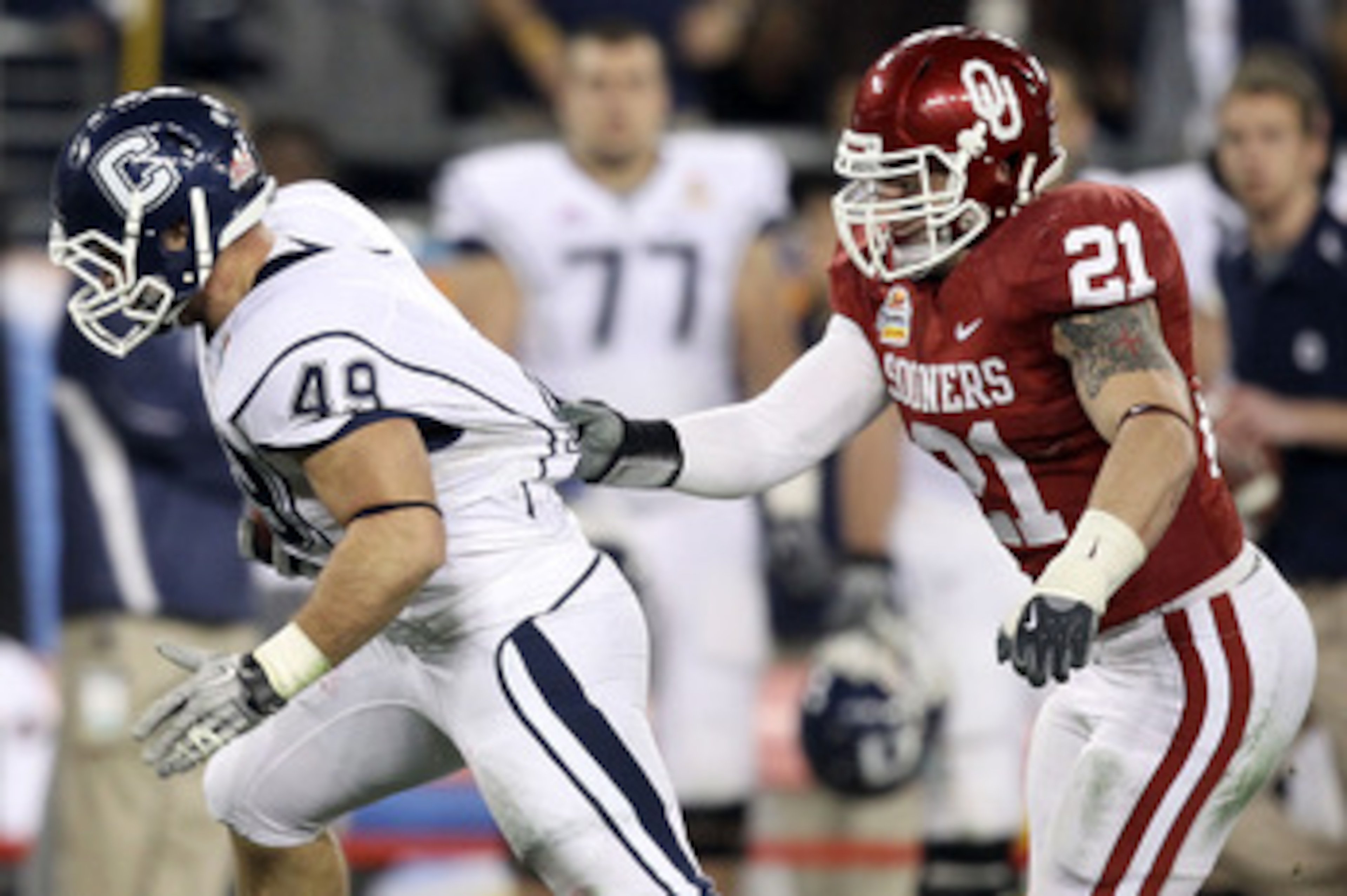 GLENDALE, AZ - JANUARY 01:  Anthony Sherman #49 of the Connecticut Huskies runs the ball as his jersey is grabbed by Tom Wort #21 of the Oklahoma Sooners in the fourth quarter during the Tostitos Fiesta Bowl at the Universtity of Phoenix Stadium on Januar