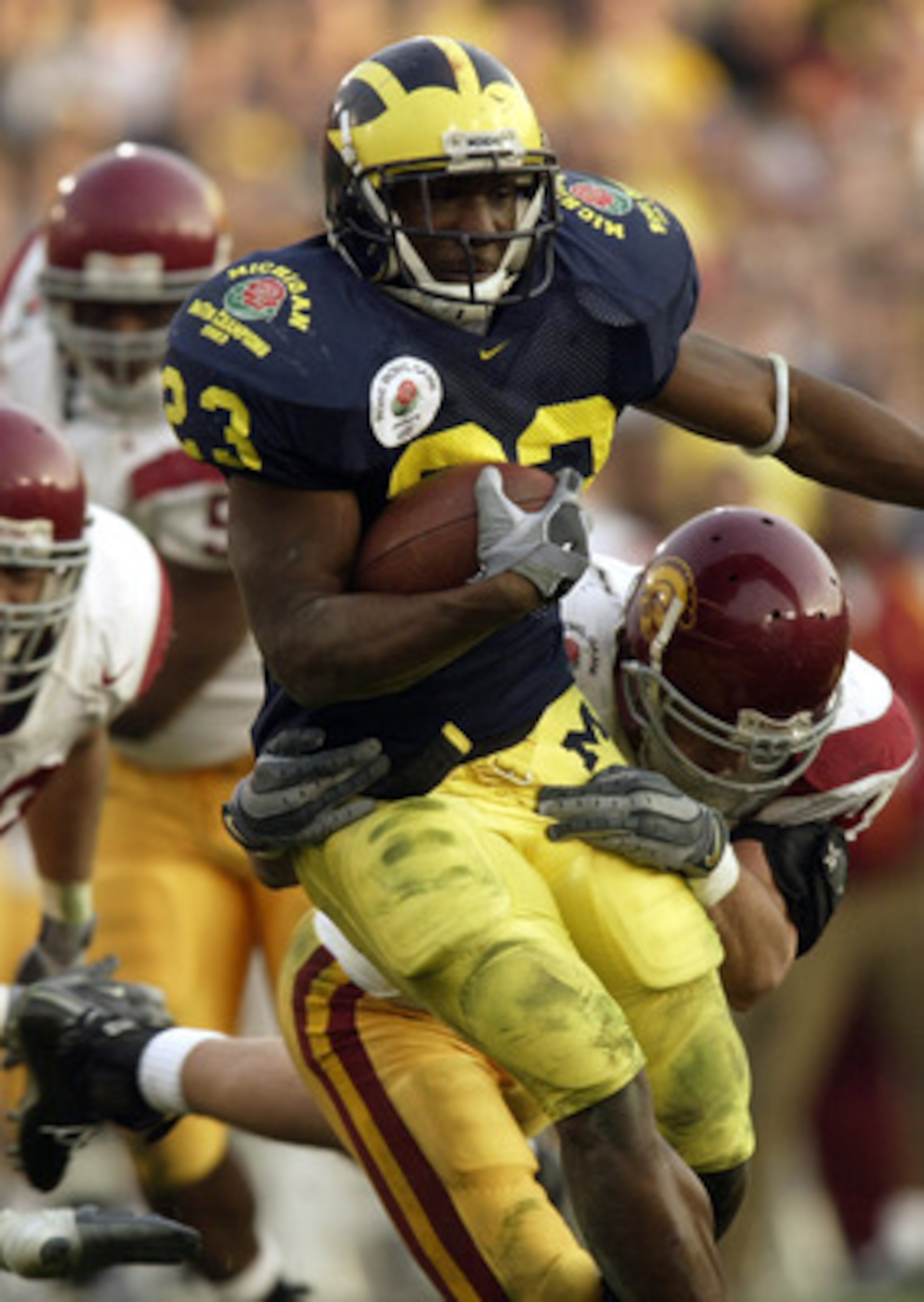 PASADENA, CA - JANUARY 1:  Running back Chris Perry #23 of the Michigan Wolverines attempts to break loose from the grasp of a USC Trojans defender during the 2004 Rose Bowl game on January 1, 2004 at the Rose Bowl in Pasadena, California. USC defeated Mi