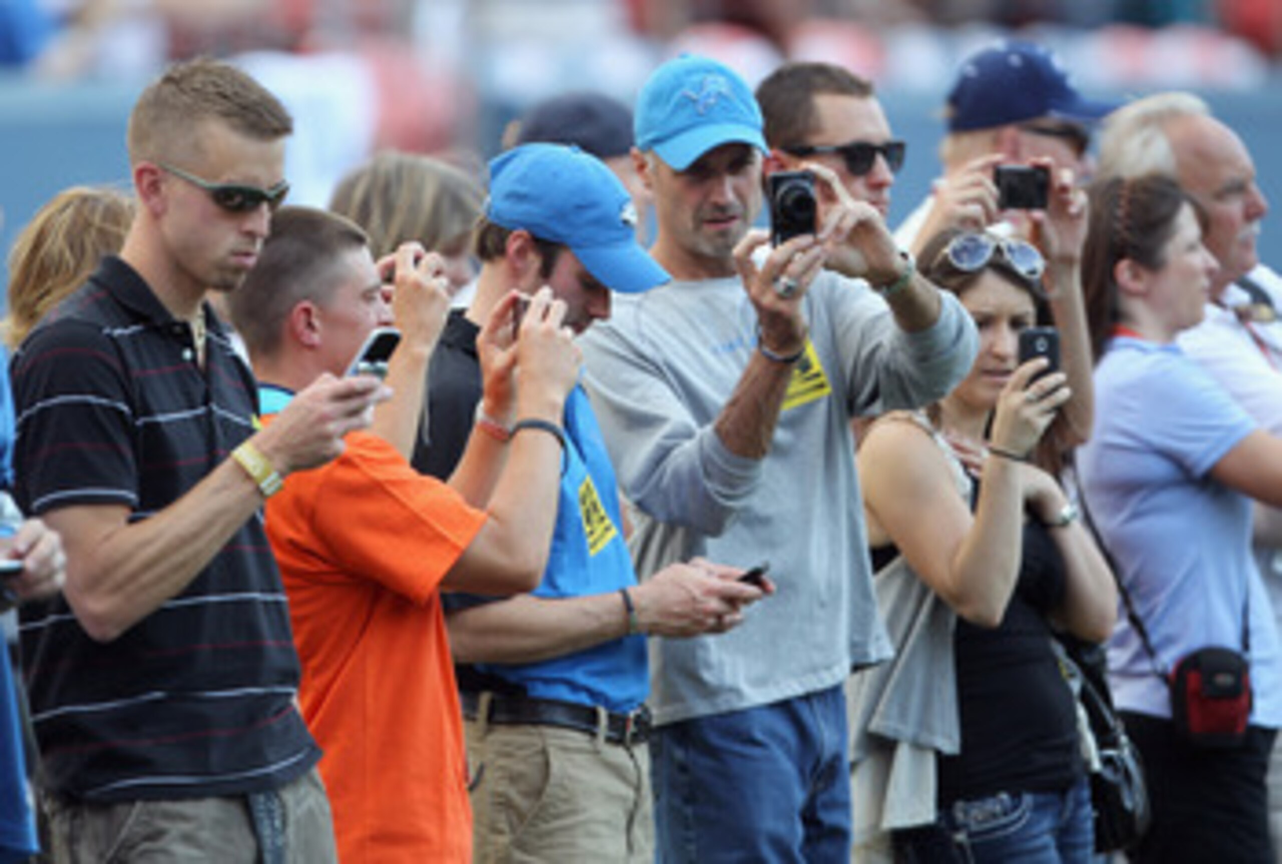 DENVER - AUGUST 21:  VIP fans on the sideline train their media capturing devices on the players during pregame warm ups as the Denver Broncos host the Detroit Lions during preseason NFL action at INVESCO Field at Mile High on August 21, 2010 in Denver, C