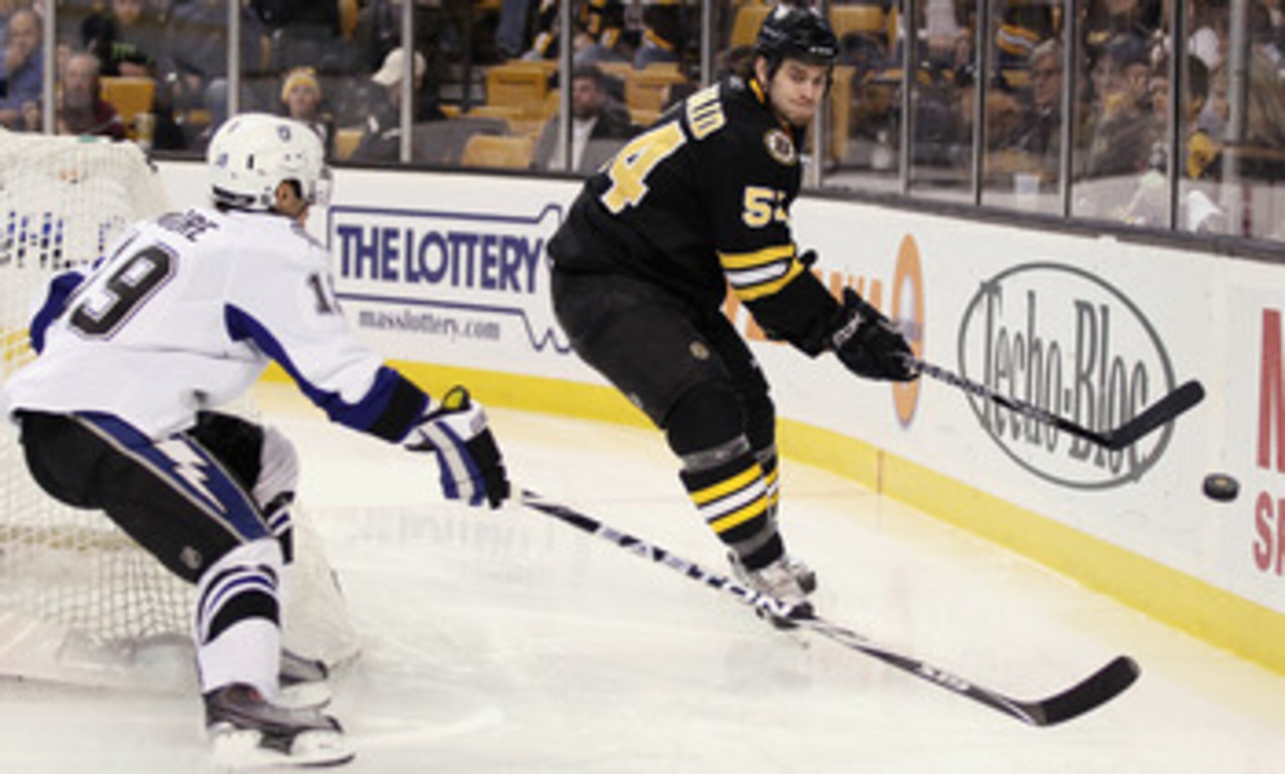 BOSTON, MA - MARCH 03:  Adam McQuaid #54 of the Boston Bruins clears the puck as Dominic Moore #19 of the Tampa Bay Lightning tries to make the steal on March 3, 2011 at the TD Garden in Boston, Massachusetts.  (Photo by Elsa/Getty Images)