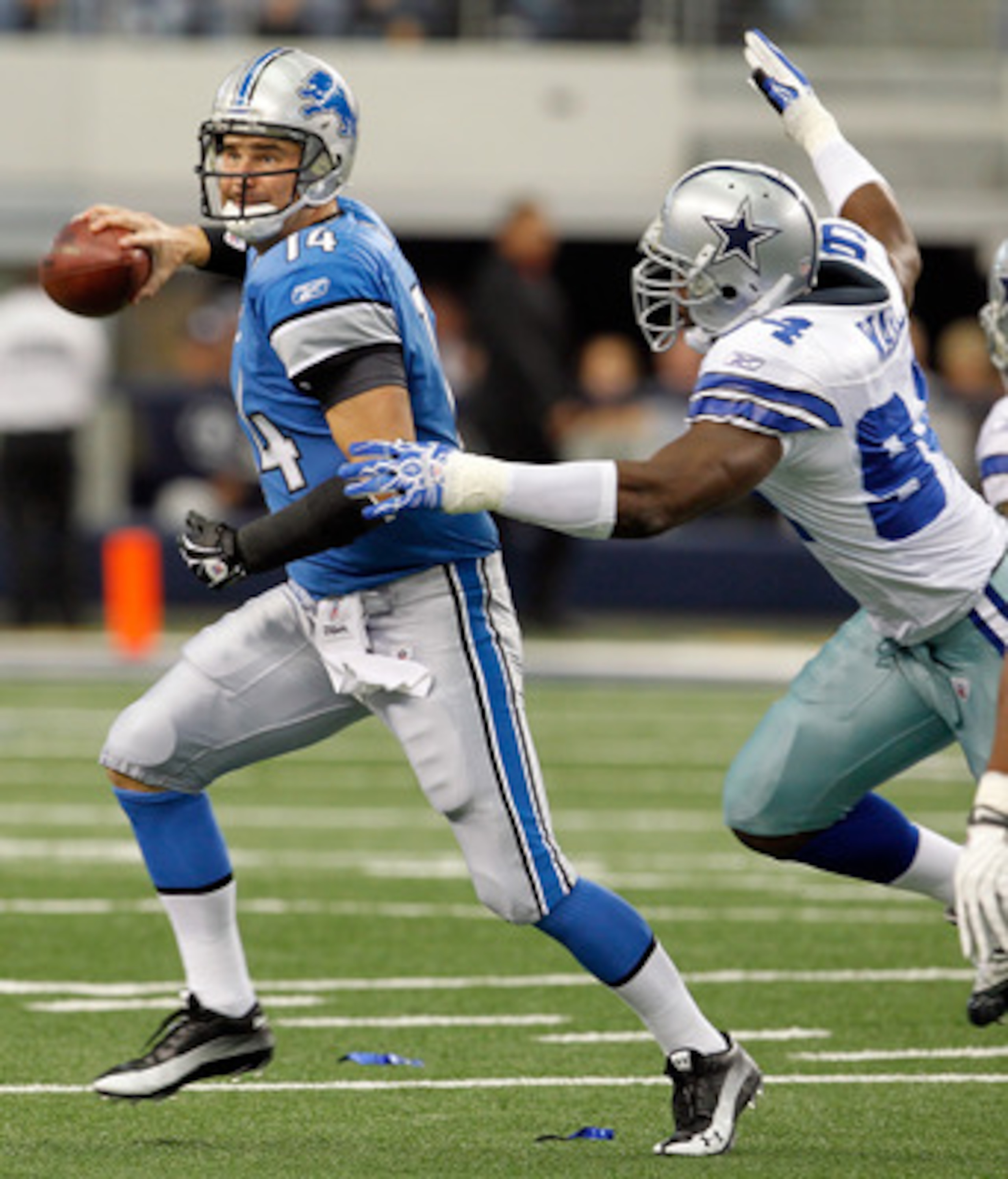 ARLINGTON, TX - NOVEMBER 21:  Quarterback Shaun Hill #14 of the Detroit Lions scrambles with the ball under pressure by Demarcus Ware #94 of the Dallas Cowboys at Cowboys Stadium on November 21, 2010 in Arlington, Texas.  The Cowboys beat the Lions 35-19.
