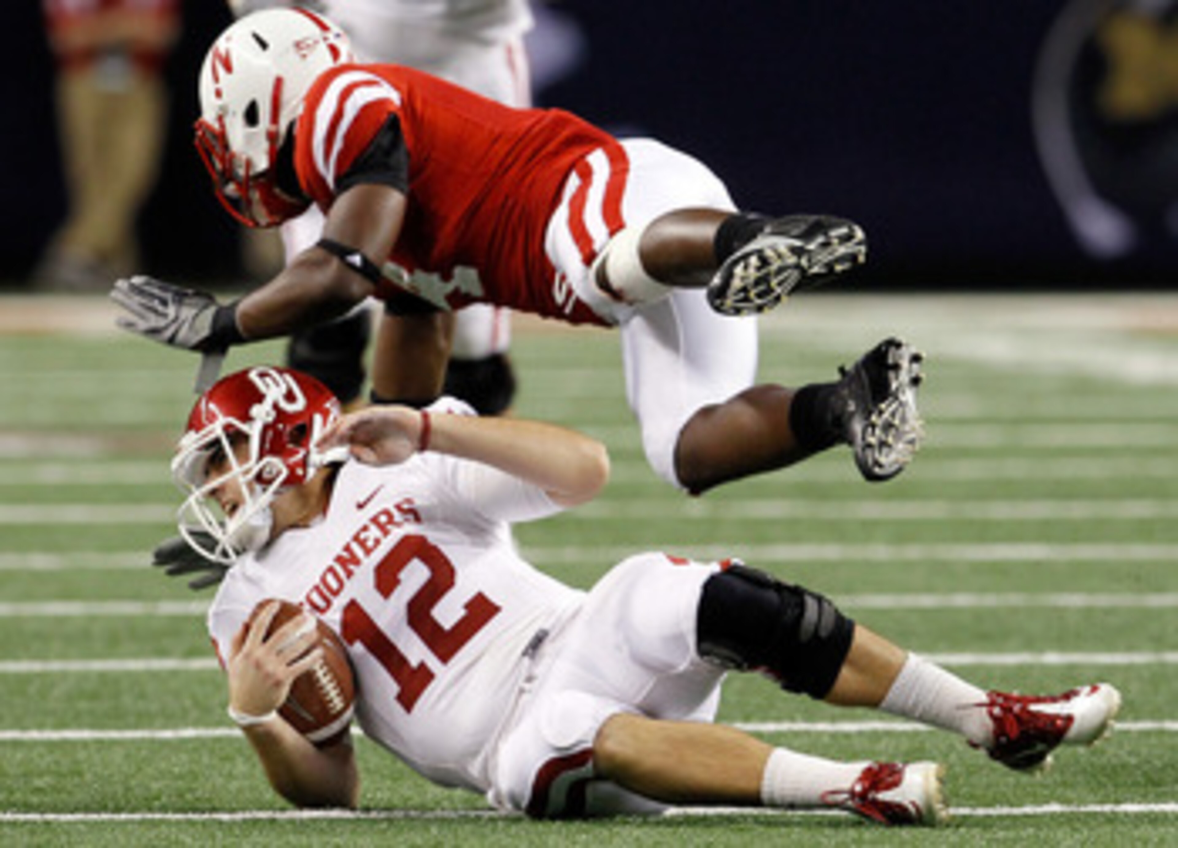 ARLINGTON, TX - DECEMBER 04:  Quarterback Landry Jones #12 of the Oklahoms Sooners slides to the turf after scrambling for a gain against Linebacker Lavonte David #4 of the Nebraska Cornhuskers at Cowboys Stadium on December 4, 2010 in Arlington, Texas.  