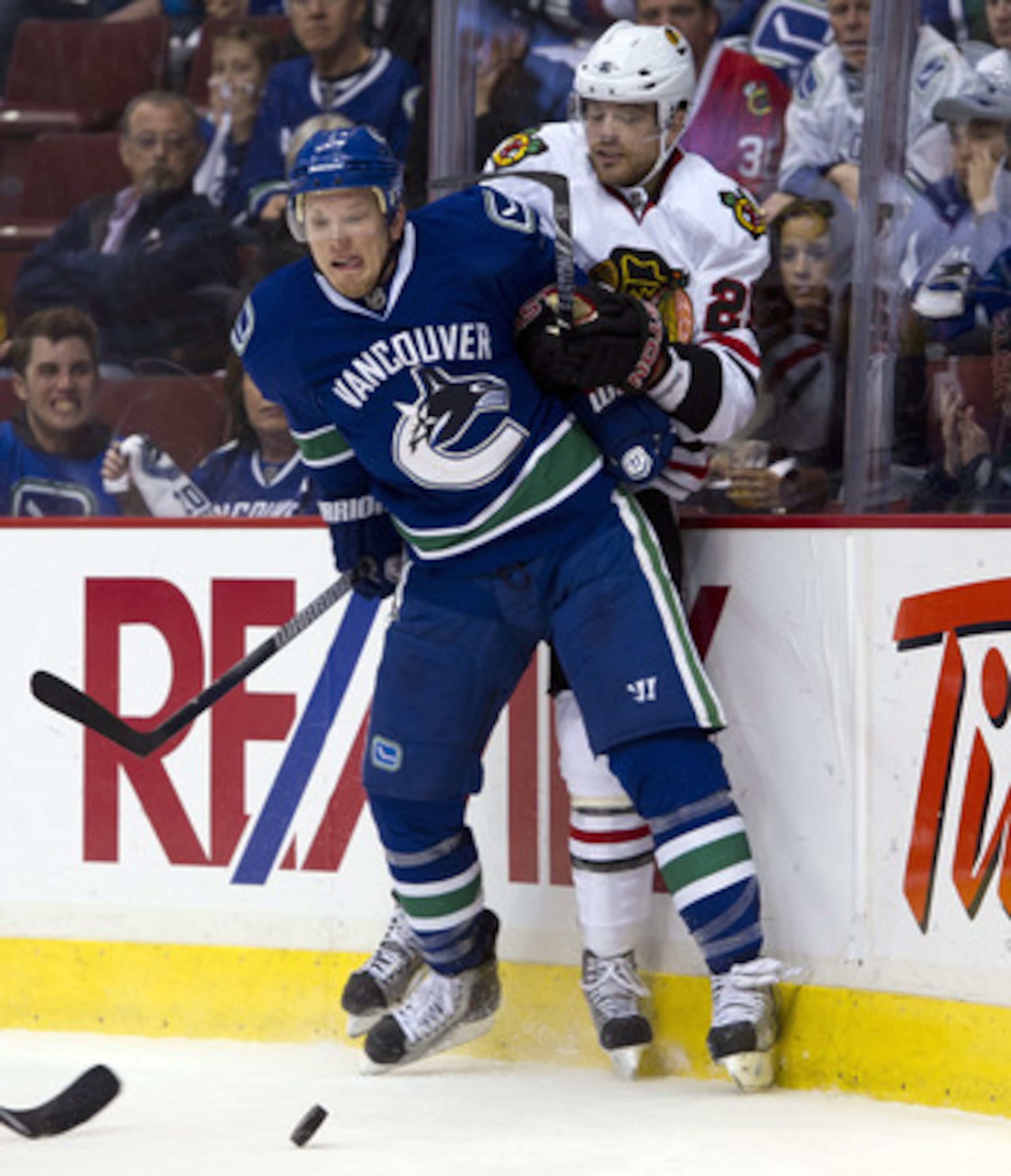 VANCOUVER, CANADA - APRIL 21: Christian Ehrhoff #5 of the Vancouver Canucks and Viktor Stalberg #25 of the Chicago Blackhawks get tangled up along the end boards during the third period in Game Five of the Western Conference Quarterfinals during the 2011