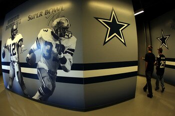 ARLINGTON, TX - OCTOBER 31:  Fans of the Dallas Cowboys walk down past a wall, with the likness's of former Cowboy players Roger Staubach #12 and Tony Dorsett along a hallway on the interior main concourse of Cowboys Stadium against the Jacksonville Jagua