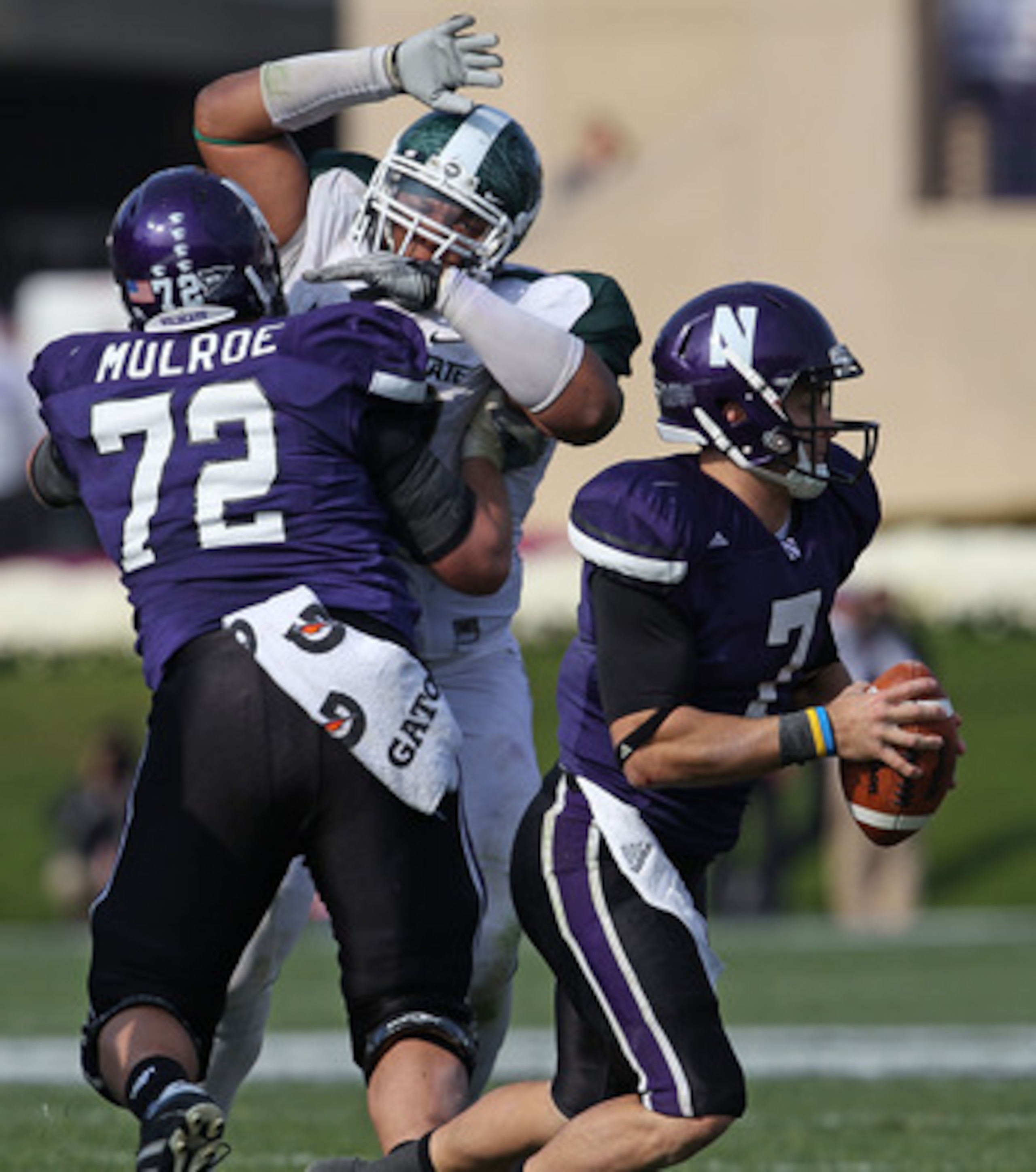 EVANSTON, IL - OCTOBER 23: Dan Persa #7 of the Northwestern Wildcats looks for a receiver as teammate Brain Mulroe #72 blocks Jerel Worthy #99 of the Michigan State Spartans at Ryan Field on October 23, 2010 in Evanston, Illinois. Michigan State defeated 