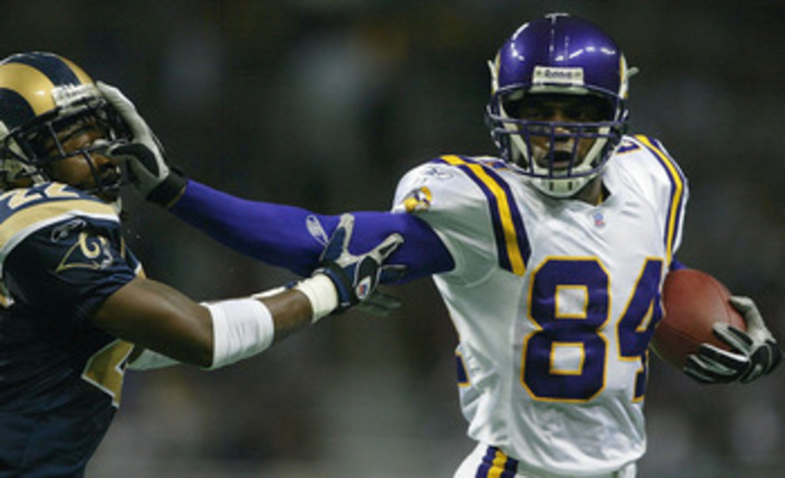 ST. LOUIS - NOVEMBER 30:  Randy Moss #84 of the Minnesota Vikings stiff arms Travis Fisher #22 of the St. Louis Rams on November 30, 2003 at the Edward Jones Dome in St. Louis, Missouri. The Rams defeated the Vikings 48-17.  (Photo by Elsa/Getty Images)