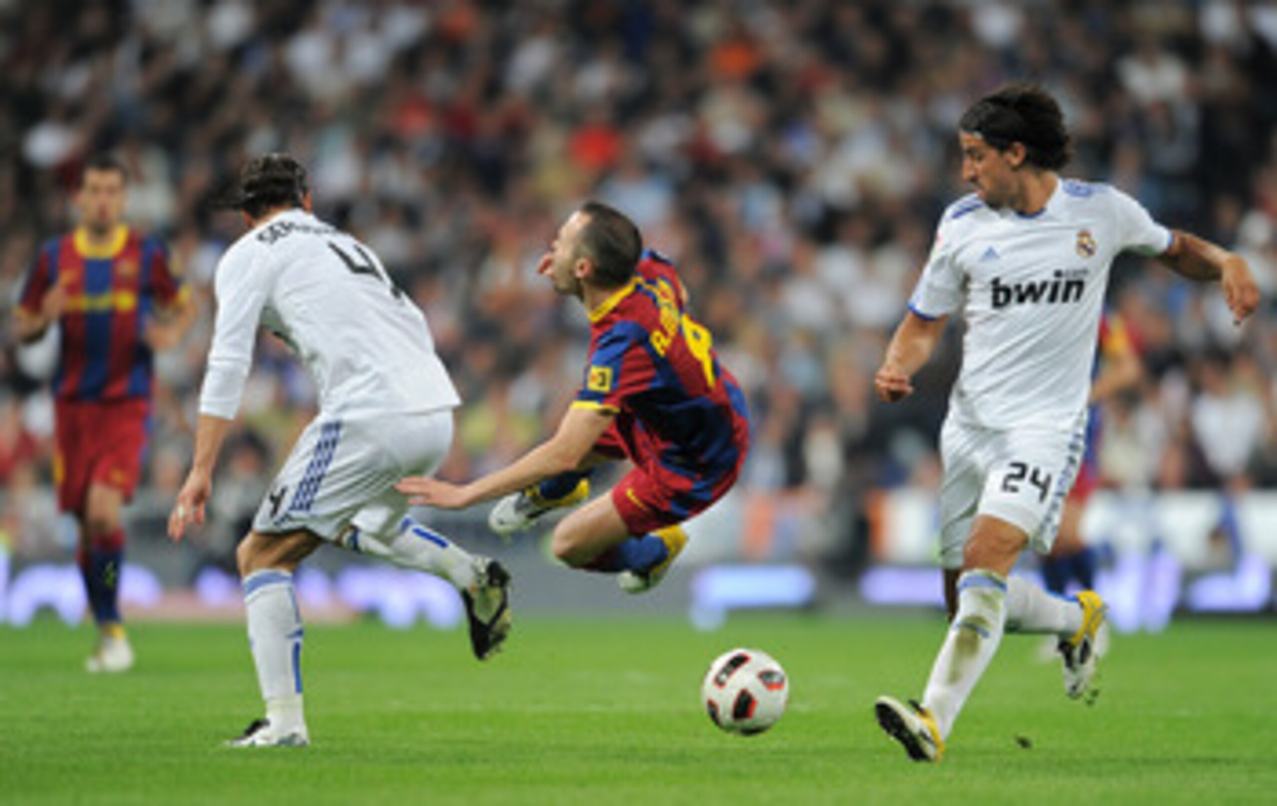 MADRID, SPAIN - APRIL 16:  Andres Iniesta (C) of Barcelona is fouled by Sergio Ramos (L) of Real Madrid as Sami Khedira of Real Madrid looks on during the la Liga match between Real Madrid and Barcelona at Estadio Santiago Bernabeu on April 16, 2011 in Ma