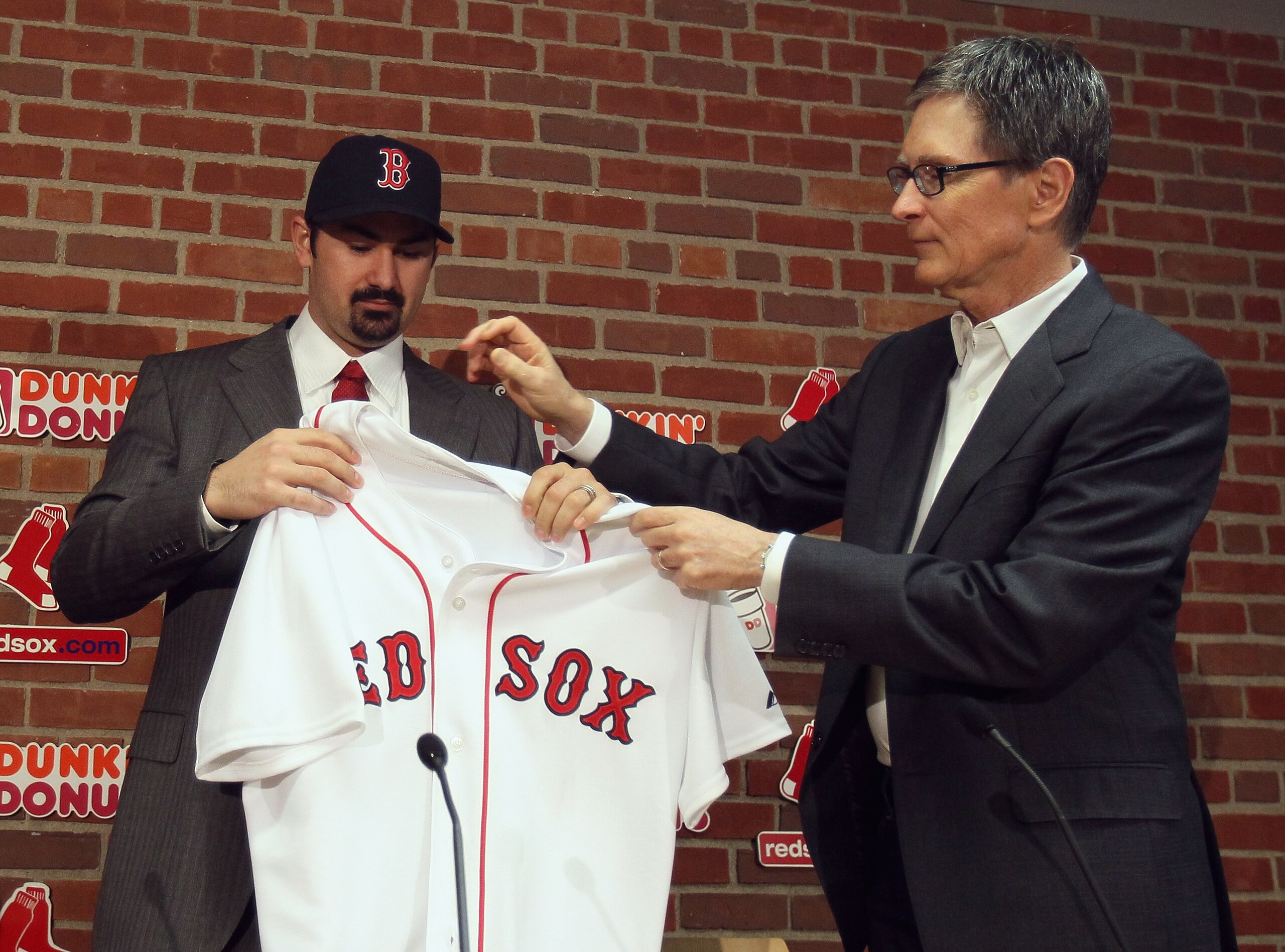 BOSTON, MA - DECEMBER 06:  Adrian Gonzalez (L) gets his jersey from principle owner John Henry during a press conference announcing that he signed with the Boston Red Sox on December 6,  2010 at Fenway Park in Boston, Massachusetts.  (Photo by Elsa/Getty