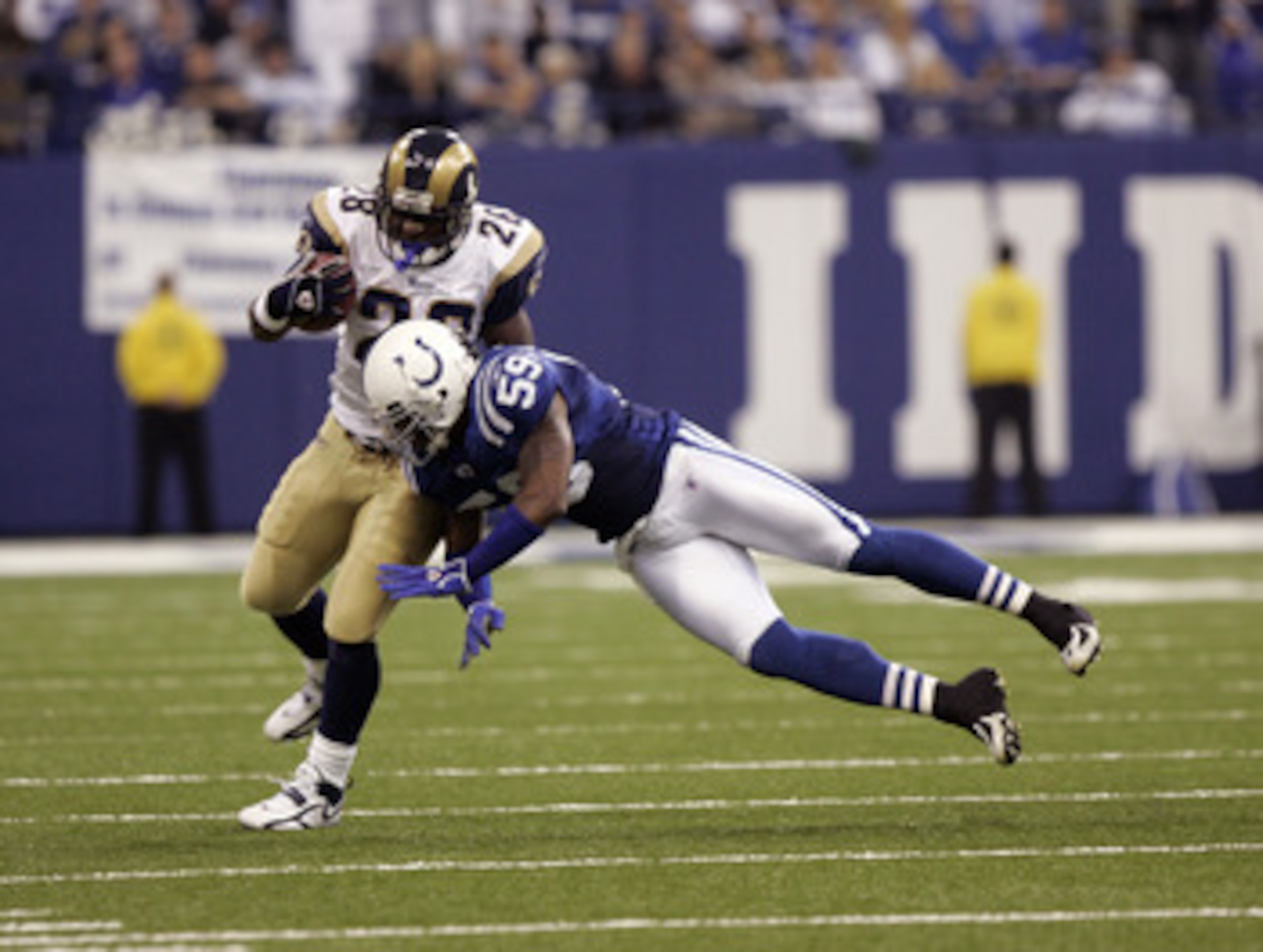 INDIANAPOLIS - OCTOBER 17:  Marshall Faulk #28 of the St. Louis Rams runs with the ball as he is tackled by Cato June #59 of the Indianapolis Colts on October 17, 2005 at the RCA Dome in Indianapolis, Indiana. The Colts defeated the Rams 45-28.  (Photo by
