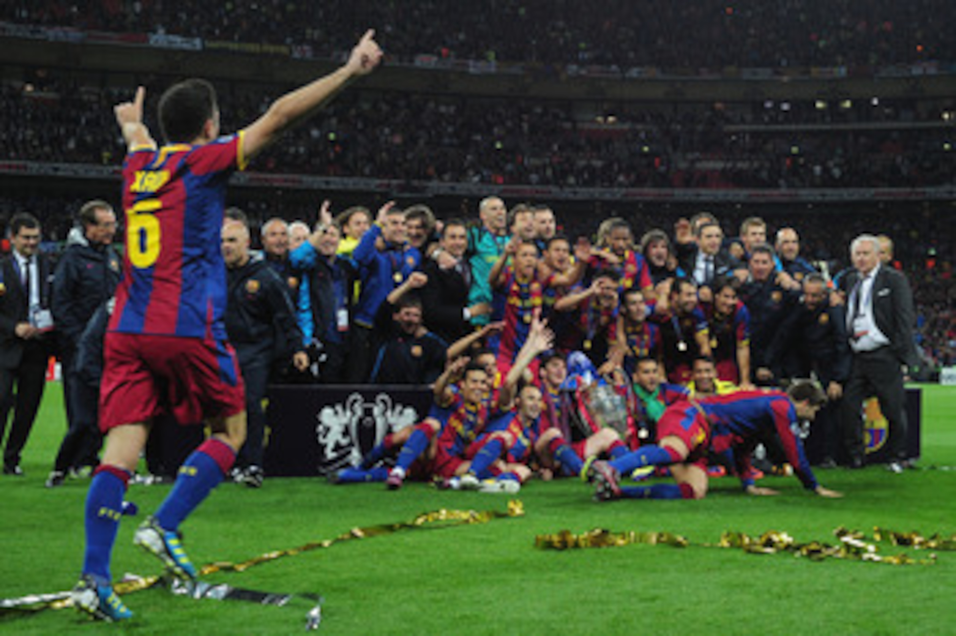 LONDON, ENGLAND - MAY 28:  Xavi (L) runs to join teammates ad Barcelona pose for photographs as they celebrate victory in the UEFA Champions League final between FC Barcelona and Manchester United FC at Wembley Stadium on May 28, 2011 in London, England.