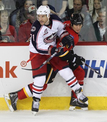 CALGARY, CANADA - MARCH 04:  Steve Staios #27 of the Calgary Flames is pinned to the boards by Chris Clark #71 of  the Columbus Blue Jackets in the third period of NHL action on March 4, 2011 at the Scotiabank Saddledome in Calgary, Alberta, Canada. (Phot