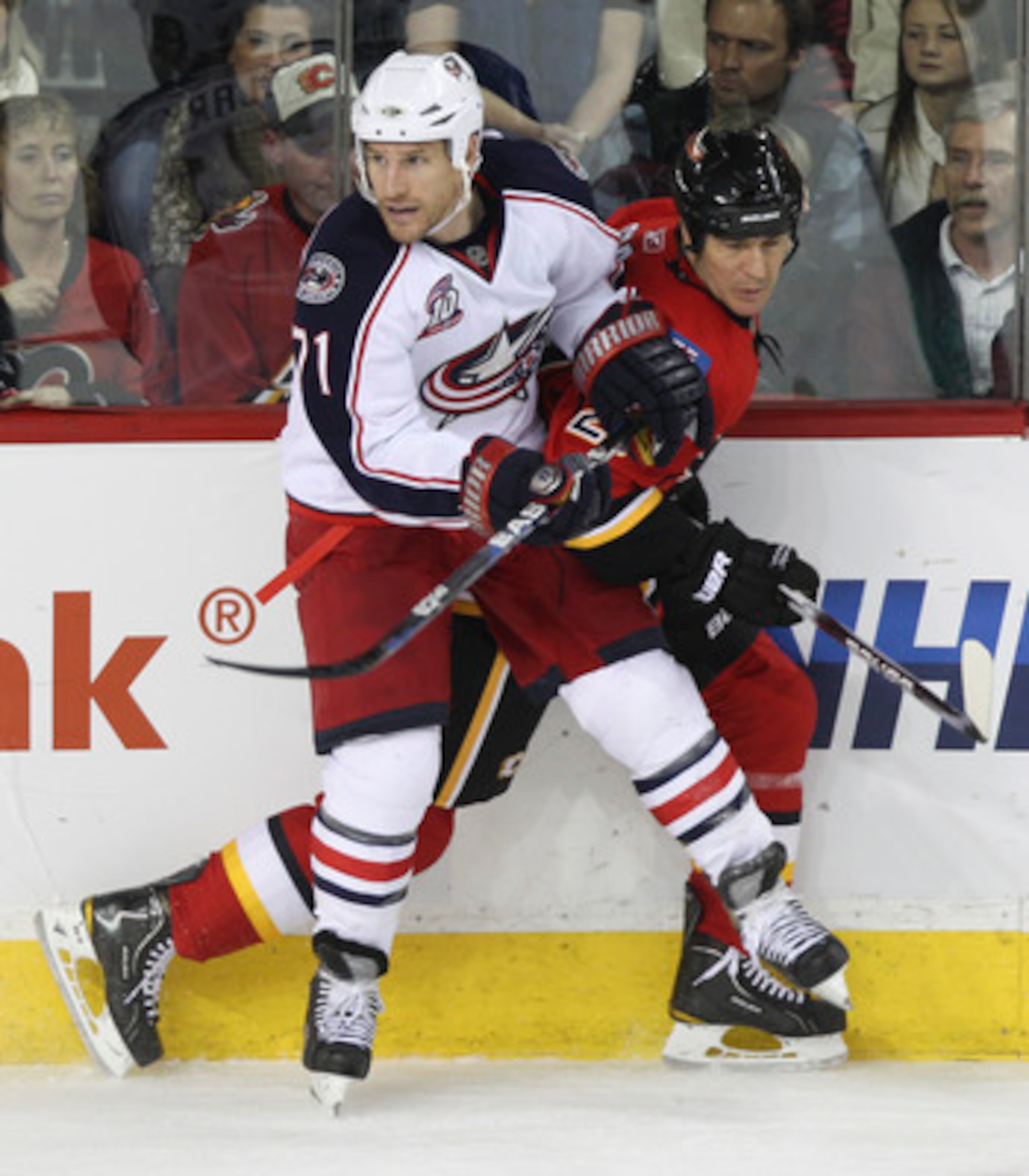 CALGARY, CANADA - MARCH 04:  Steve Staios #27 of the Calgary Flames is pinned to the boards by Chris Clark #71 of  the Columbus Blue Jackets in the third period of NHL action on March 4, 2011 at the Scotiabank Saddledome in Calgary, Alberta, Canada. (Phot