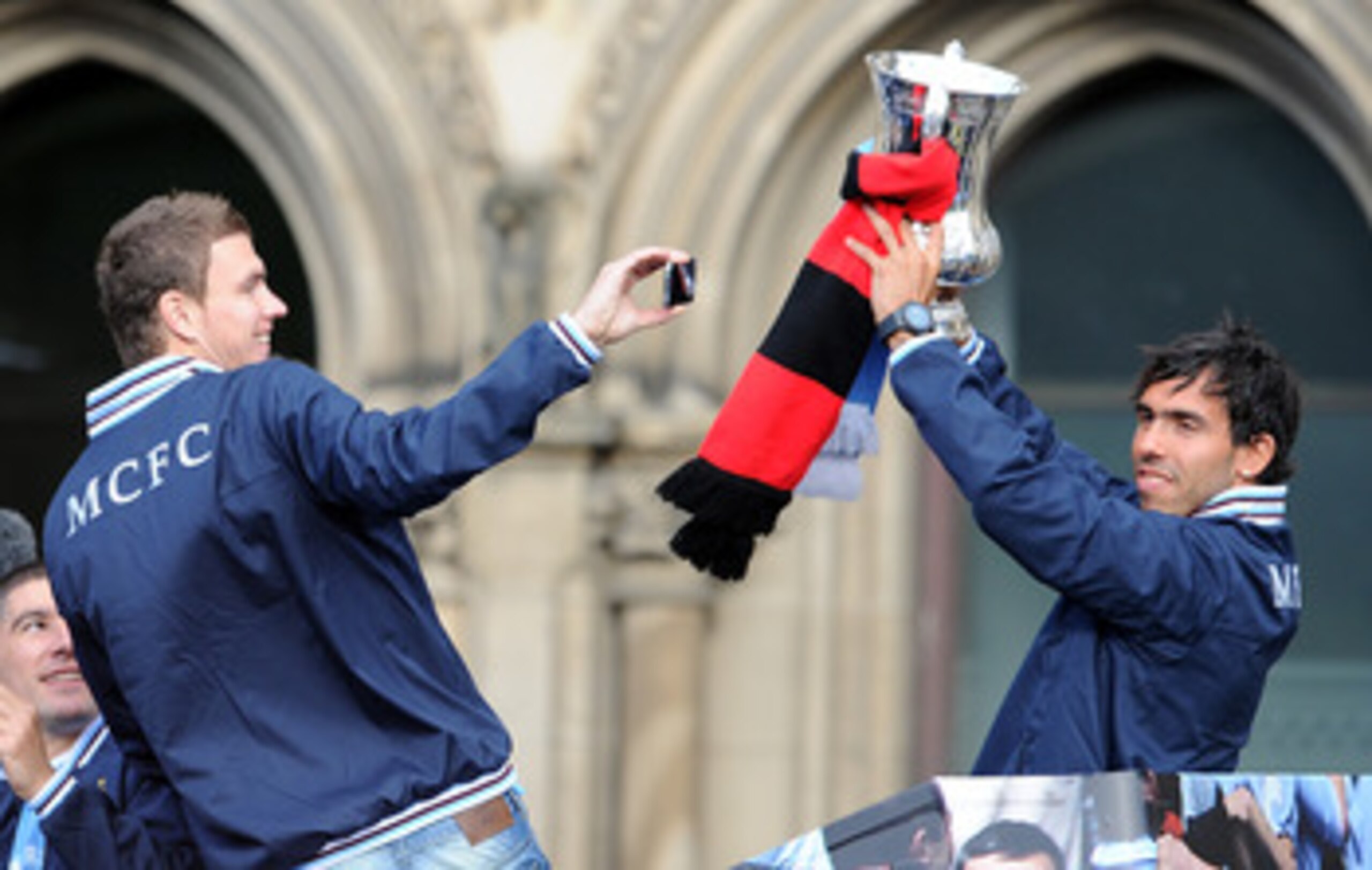 MANCHESTER, ENGLAND - MAY 23:  Carlos Tevez of Manchester City lifts the FA Cup as team-mate Edin Dzeko(L) films him on his mobile phone during the Manchester City FA Cup Winners Parade at Manchester Town Hall on May 23, 2011 in Manchester, United Kingdom