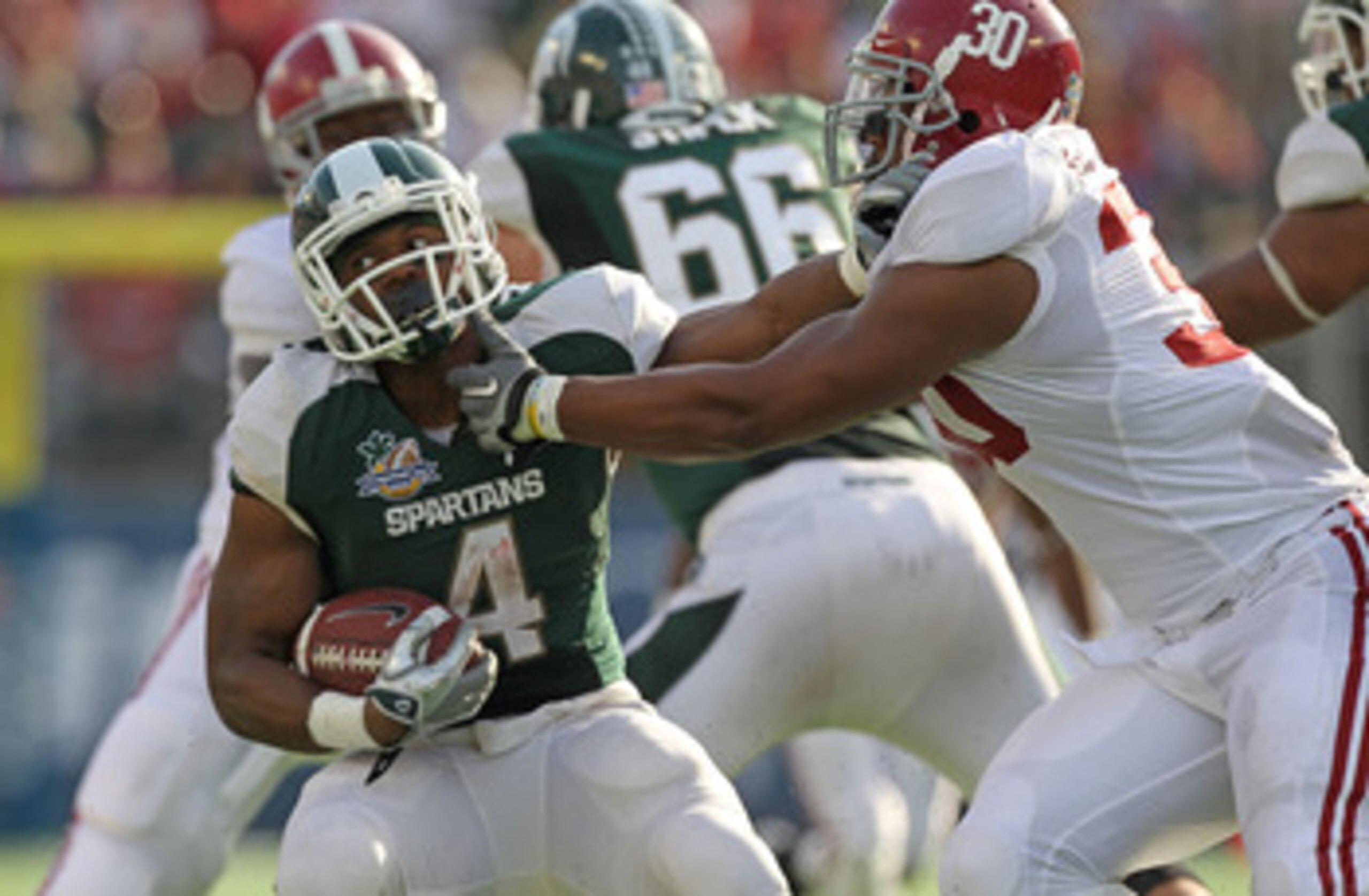 ORLANDO, FL - JANUARY 01:  Edwin Baker #4 of the Michigan State Spartans stiff arms Dont'a Hightower #30 of the Alabama Crimson Tide during the Capitol One Bowl at the Florida Citrus Bowl on January 1, 2011 in Orlando, Florida.  (Photo by Mike Ehrmann/Get